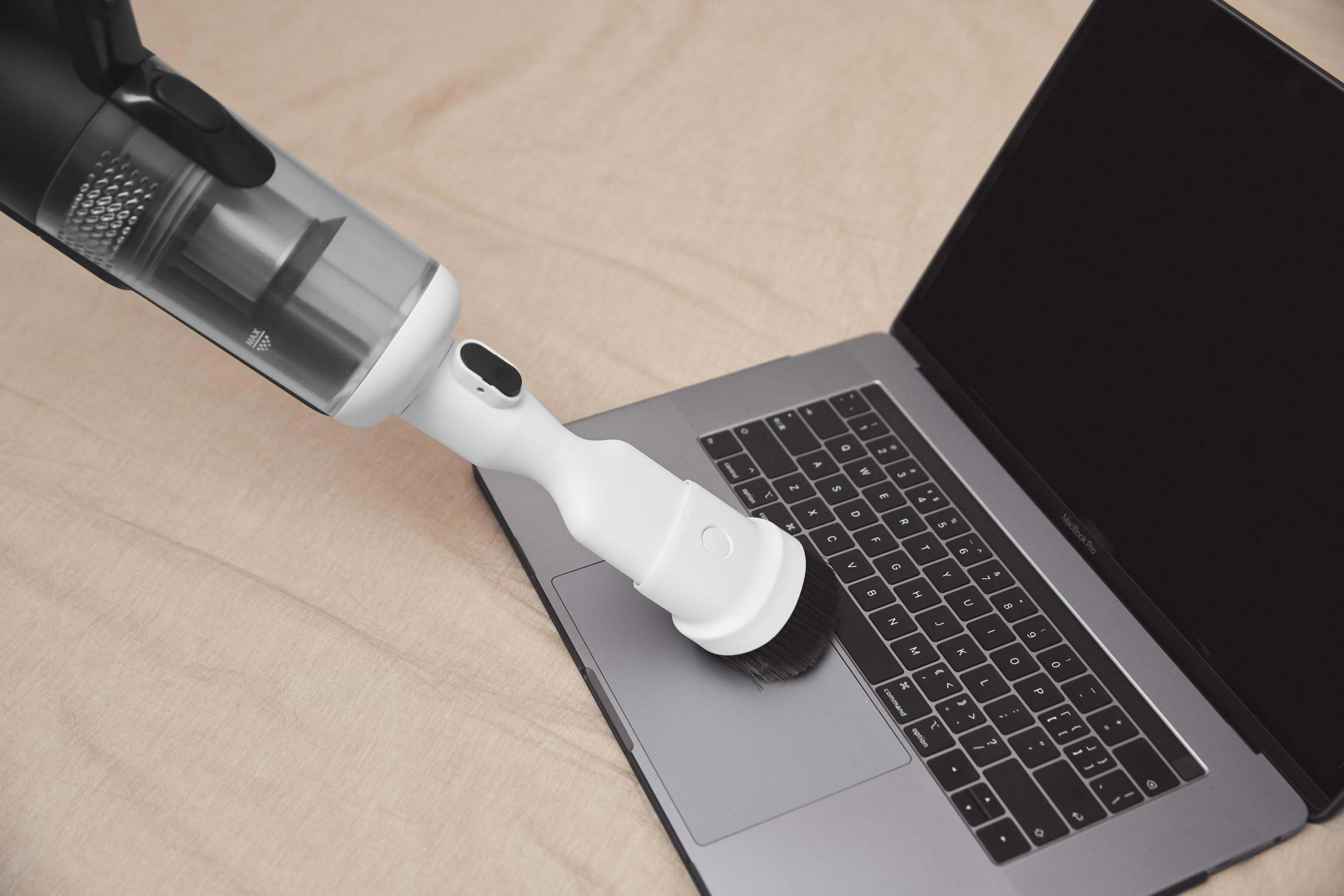 Ein Handstaubsauger reinigt eine Laptop-Tastatur. Der Hintergrund zeigt eine Holzoberfläche.