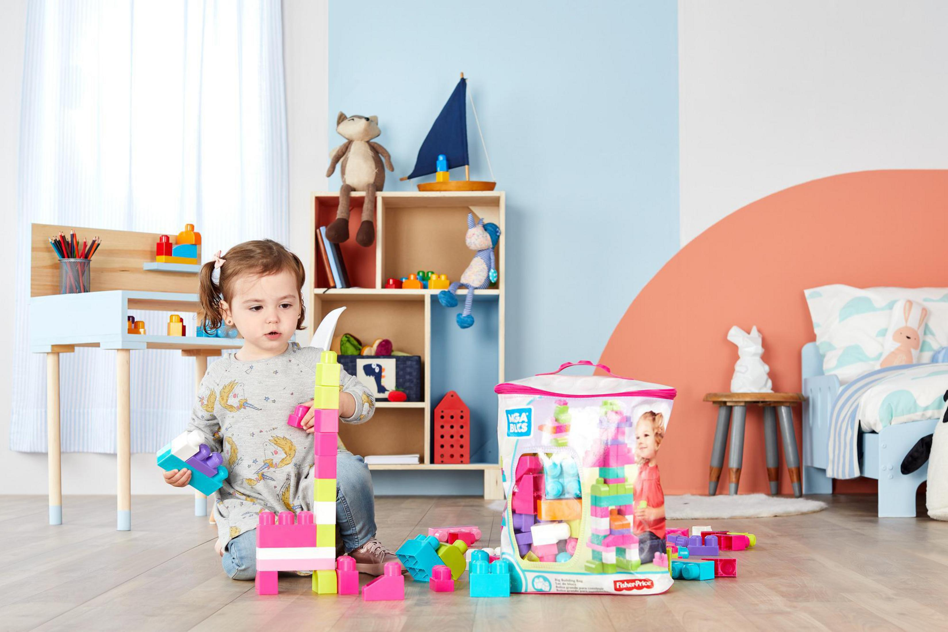 Dziewczynka bawiąca się klockami. Zabawki na półkach. Kolorowe klocki i przezroczysta torba.