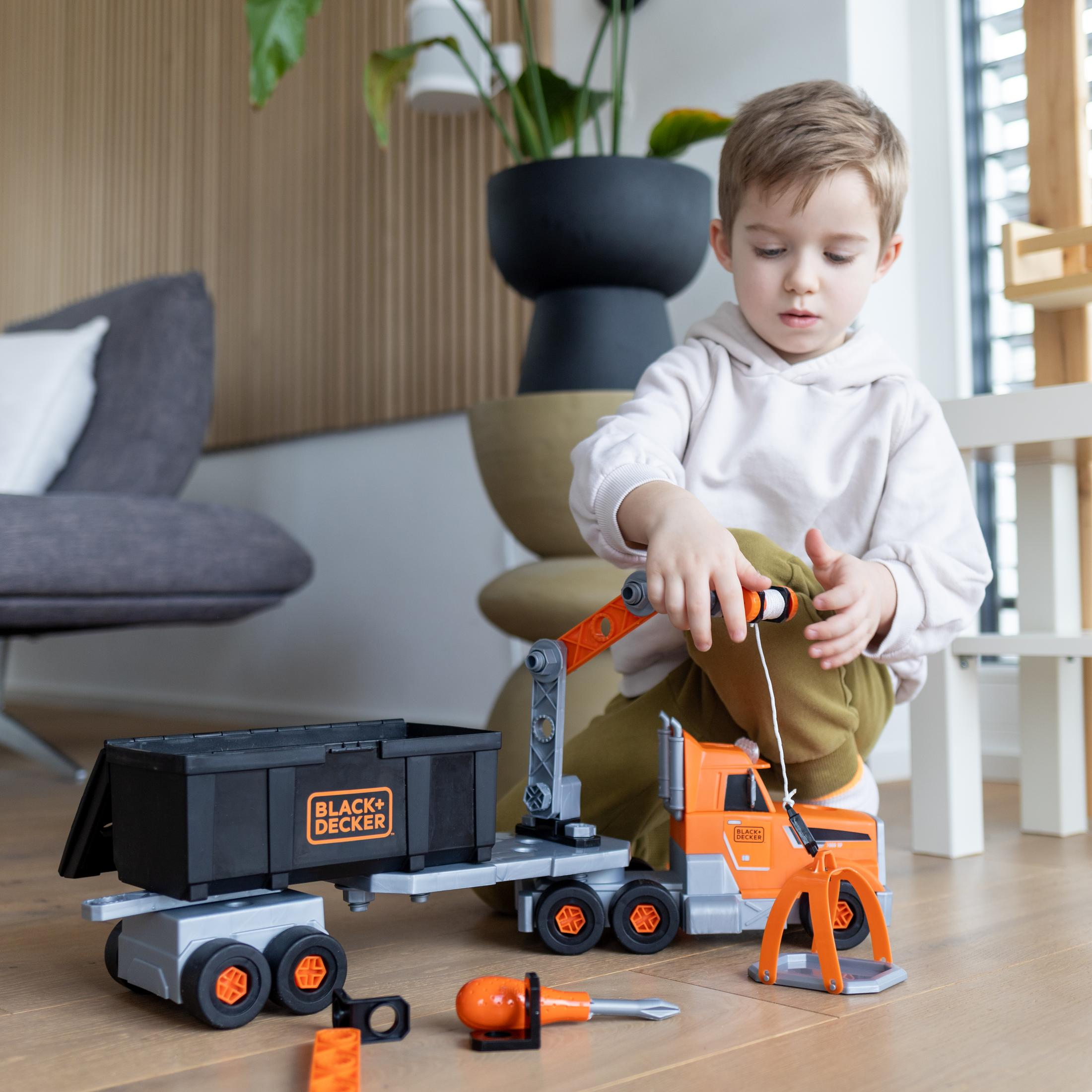 Dziecko bawiące się żurawiem i ciężarówką Black+Decker na drewnianej podłodze.