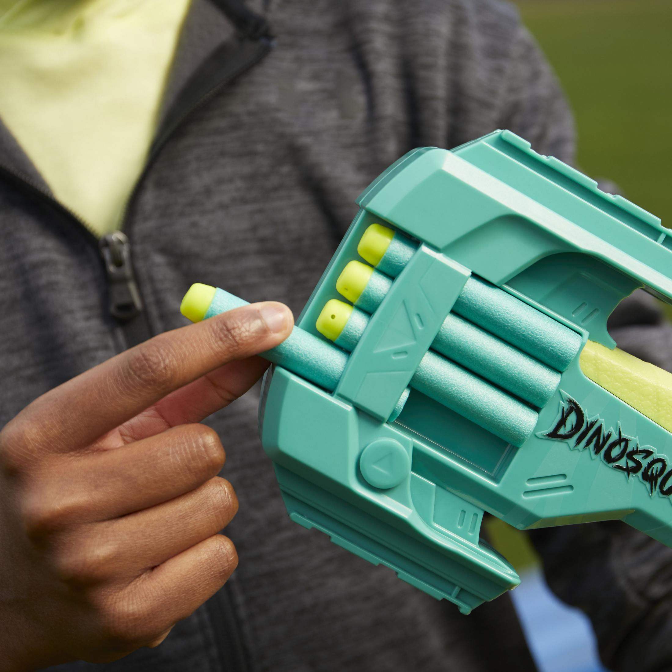 Mano de niño inserta dardo en pistola de juguete verde y azul "Dinosquad".