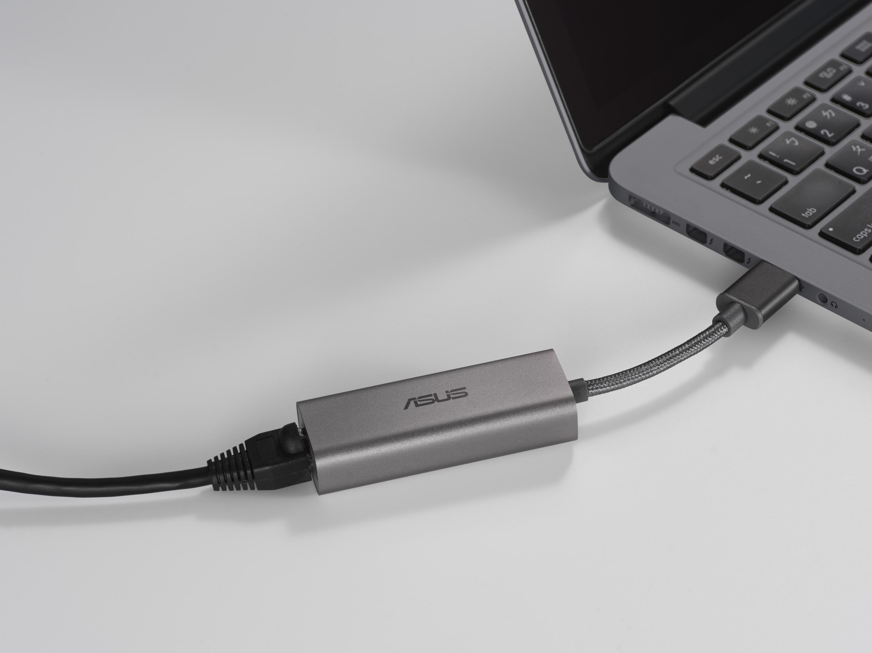 Ein ASUS USB-Adapter, der mit einem Laptop und einem schwarzen Kabel auf einer weißen Oberfläche verbunden ist.