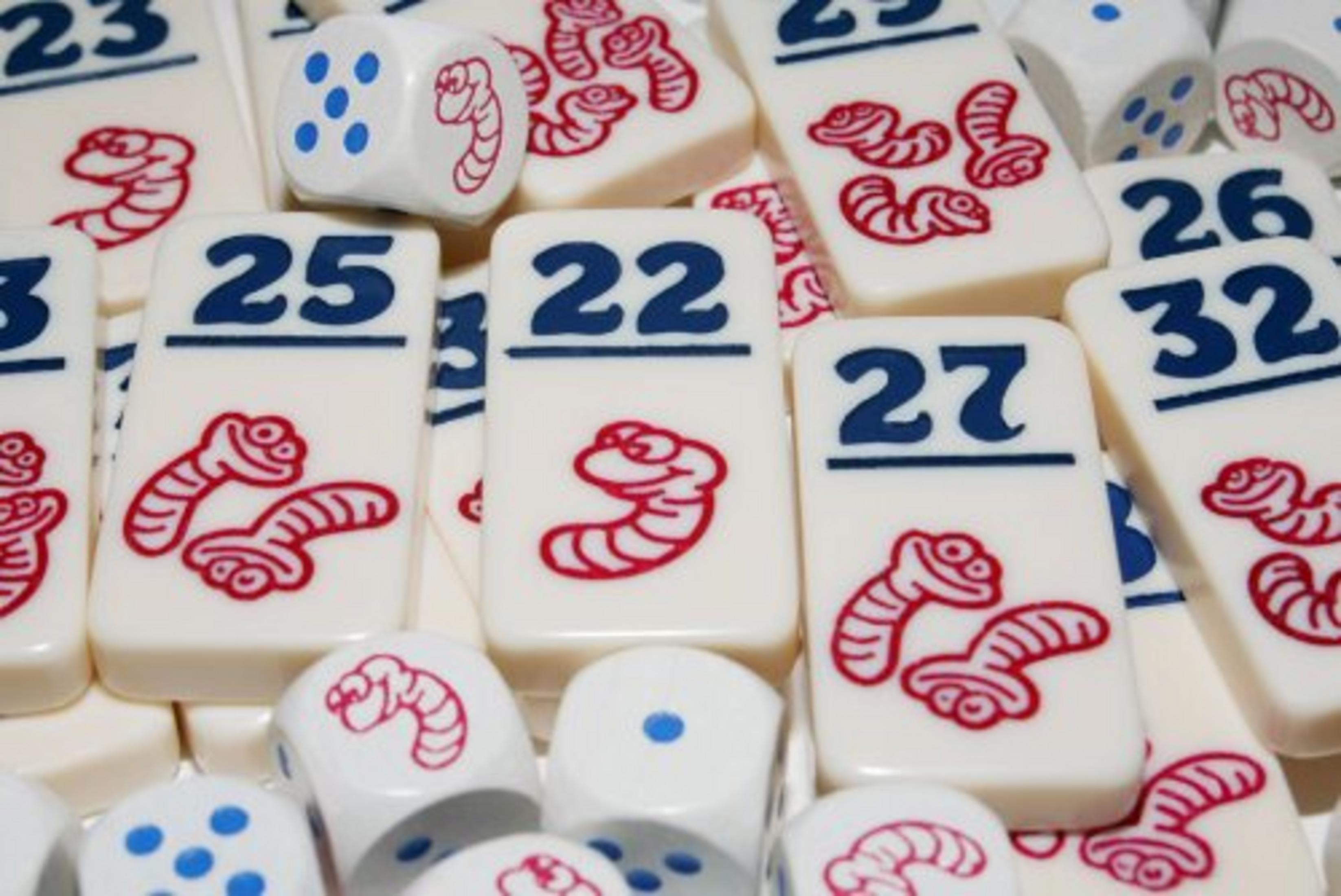 Nahaufnahme von Würfeln und Spielsteinen eines Brettspiels, mit Zahlen und Würmern.