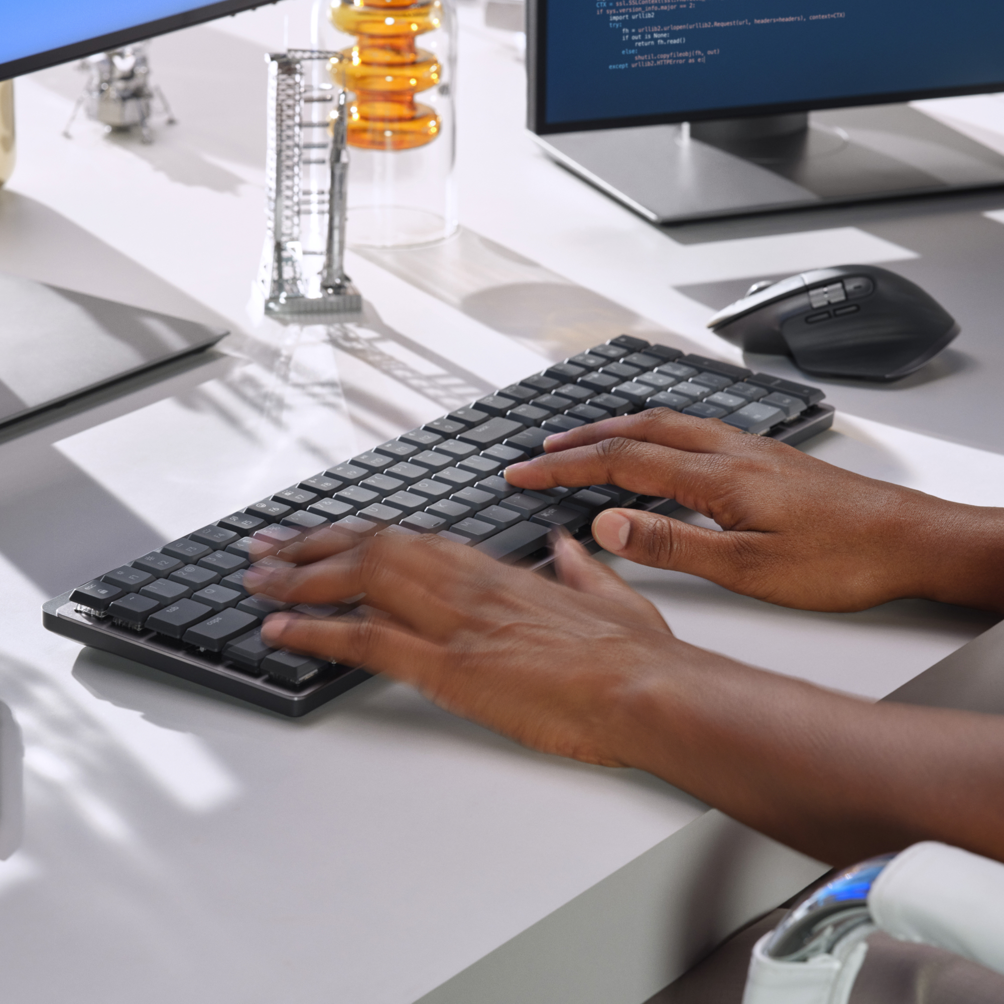 Ręce piszące na klawiaturze. Mysz, monitory i sprzęt laboratoryjny w tle.