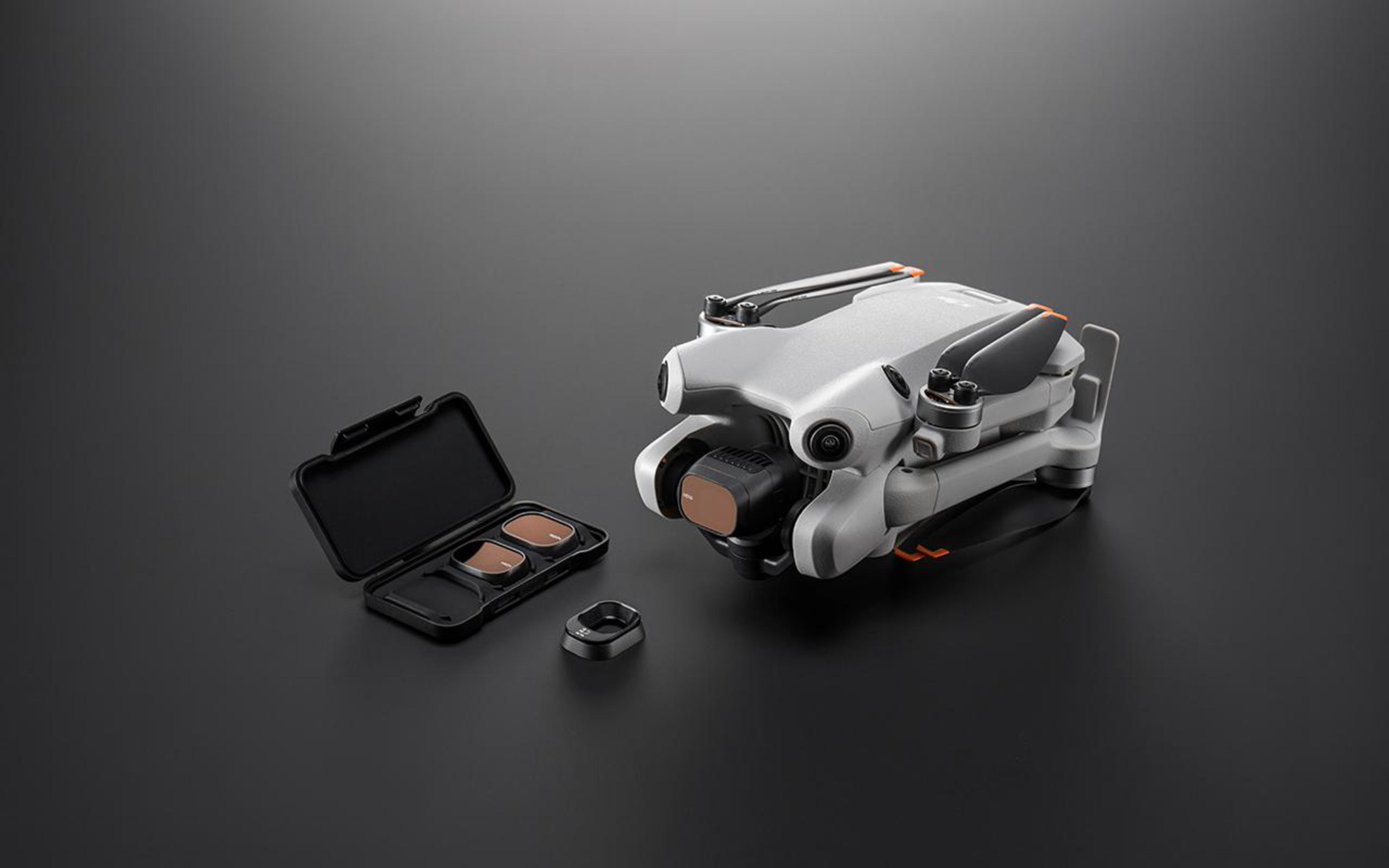 Un dron plateado con cámara y filtros sobre una superficie gris oscura.