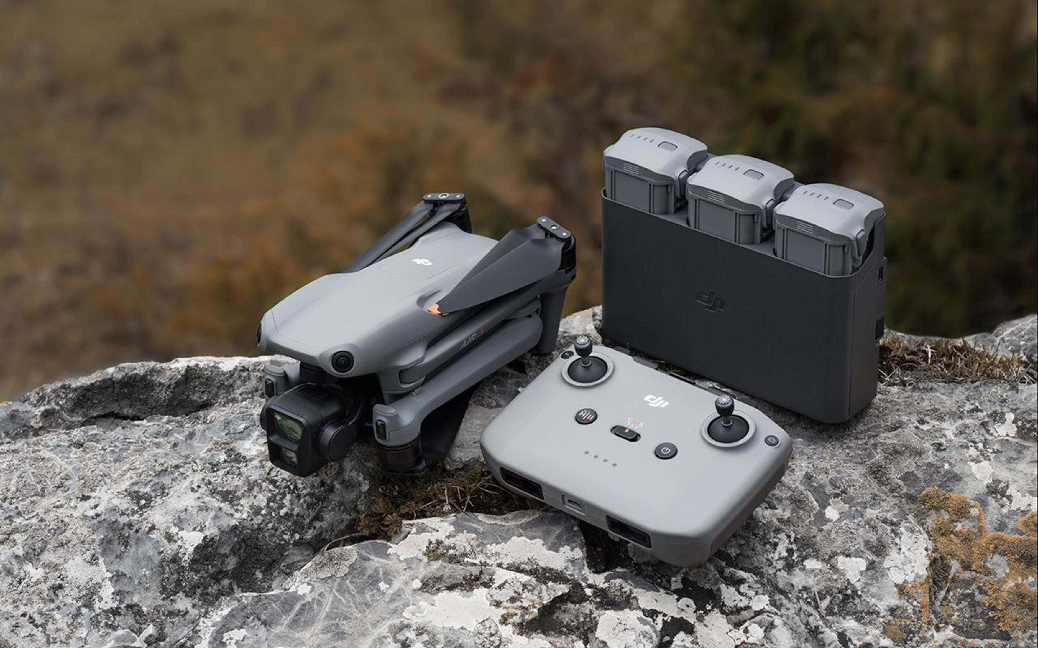 Eine graue Drohne, ein Controller und eine Ladestation liegen auf einem Felsen. Der Hintergrund ist unscharf.
