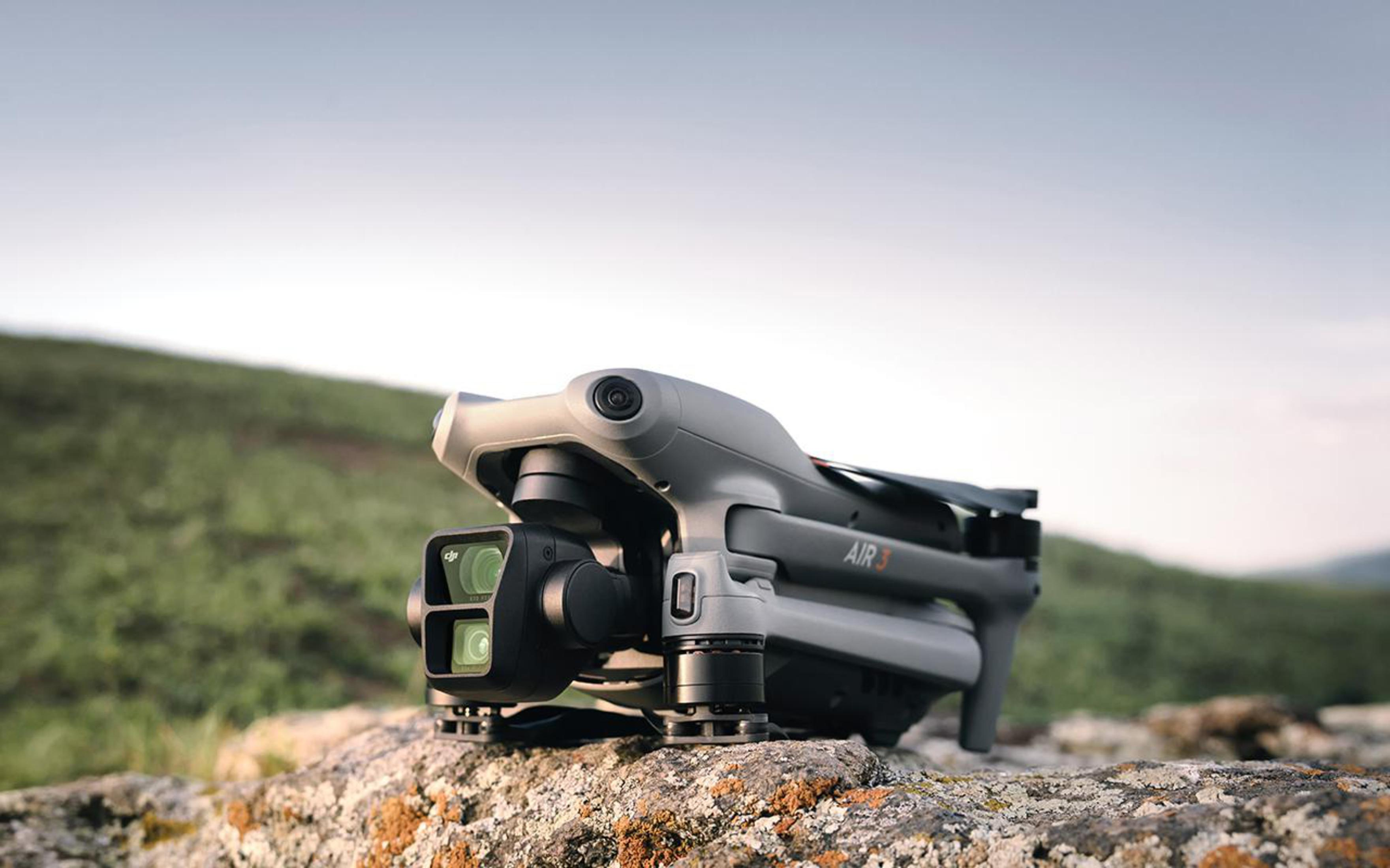 Srebrno-szary dron spoczywa na skale, z rozmytym zielonym polem w tle.