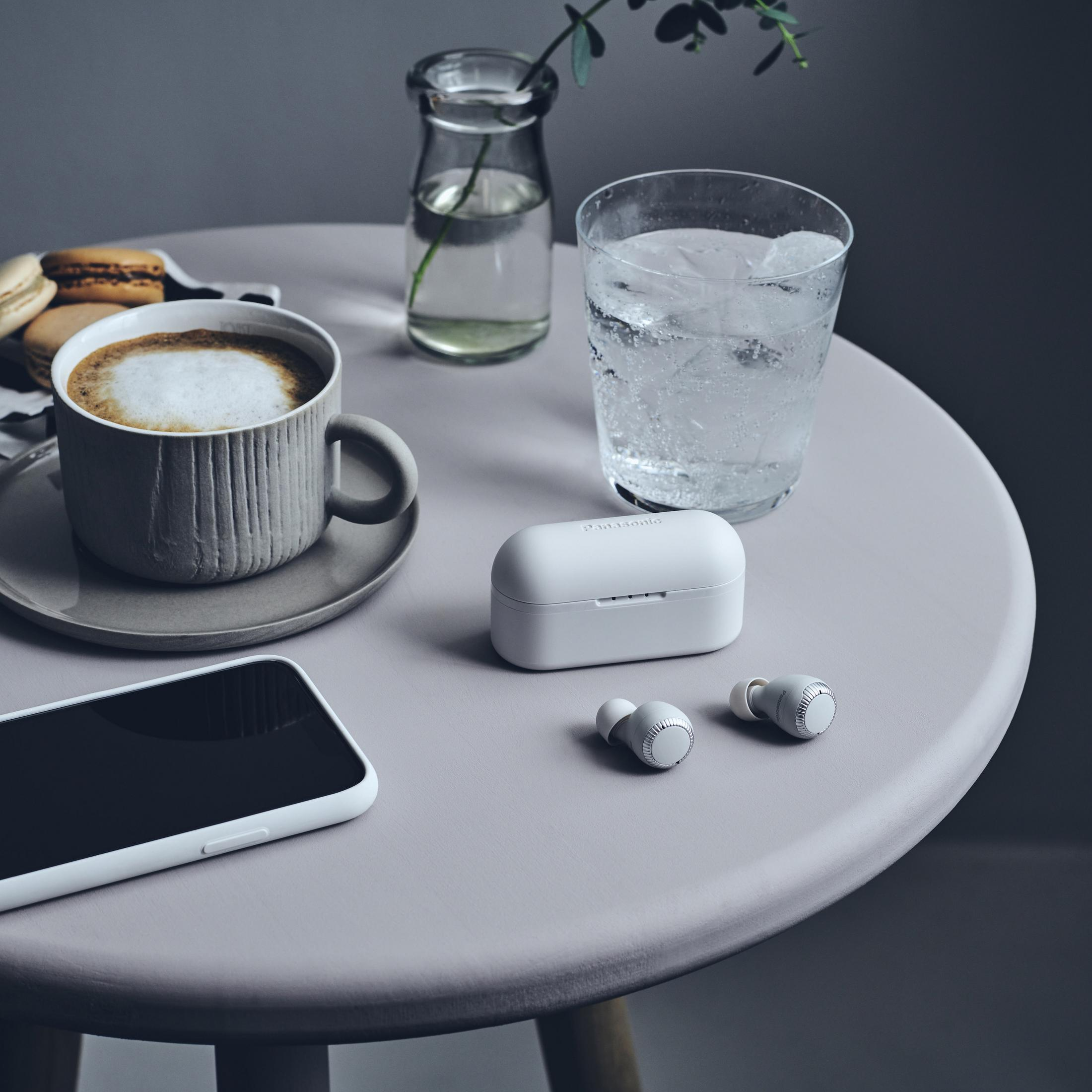 Tisch mit Kaffee, Kopfhörern, Telefon und Wasserglas. Macarons sichtbar.