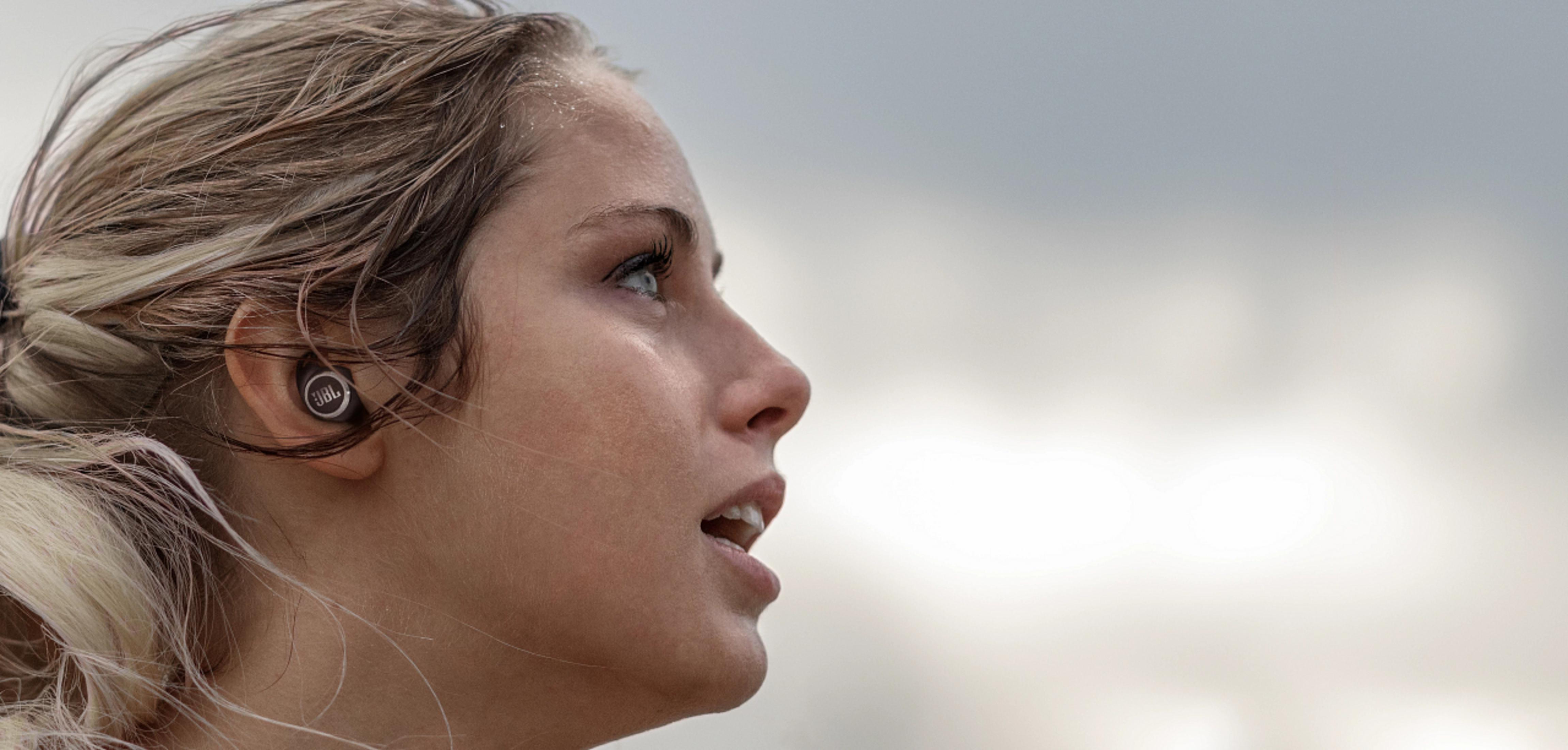 Kobieta ze słuchawkami w profilu patrząca w górę. Tło to pochmurne niebo.