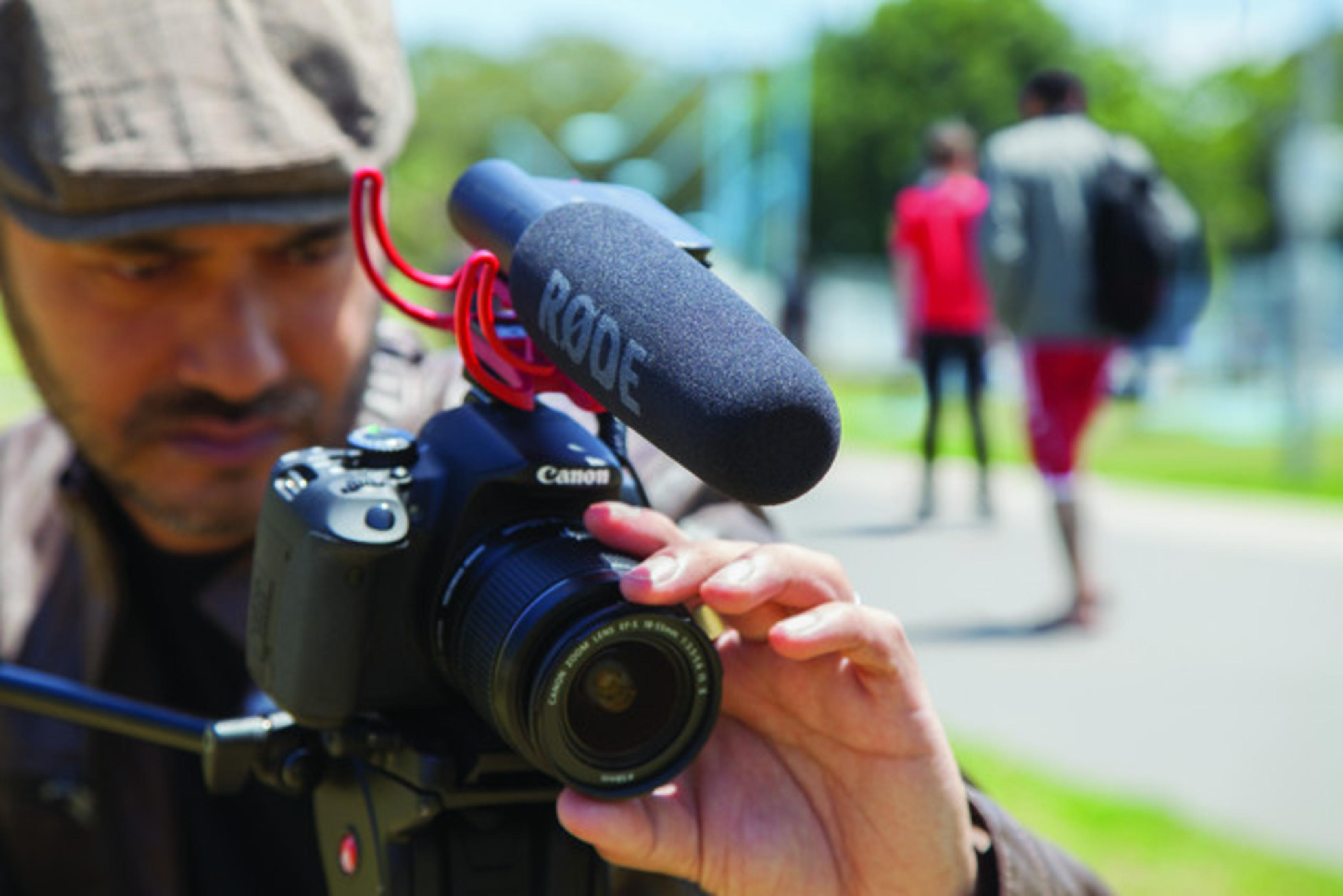 Mann filmt mit einer Canon Kamera und RODE Mikrofon. Verschwommener Hintergrund.