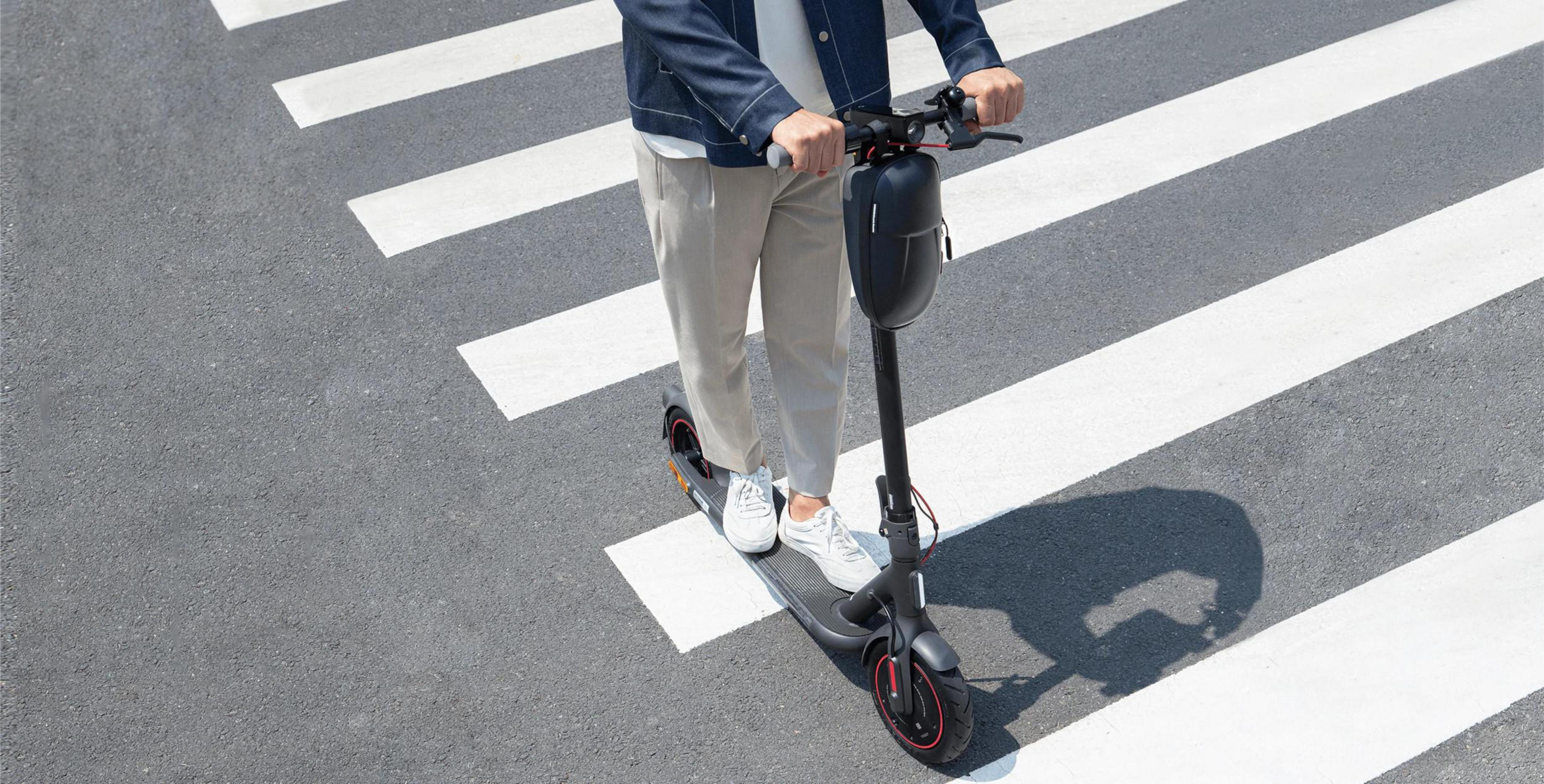 Person fährt mit einem Roller auf einem Zebrastreifen. Asphalt-Hintergrund.