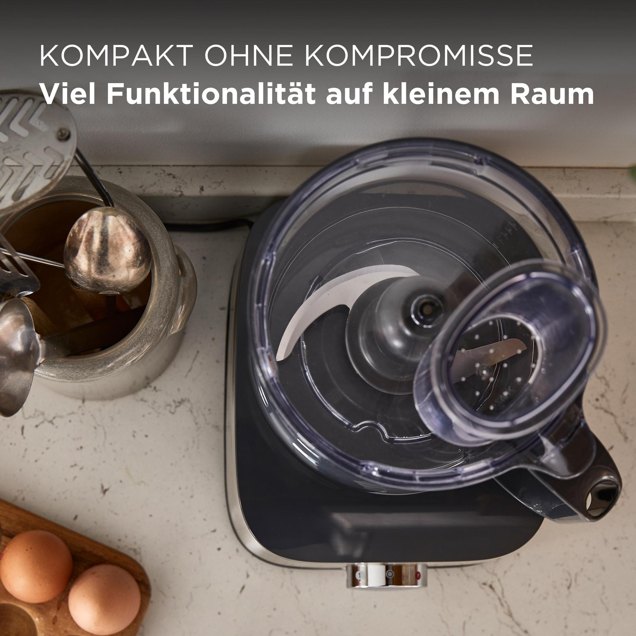 Küchenmaschine mit klarer Schüssel, Klinge und Text oben. Eier sind vorne.
