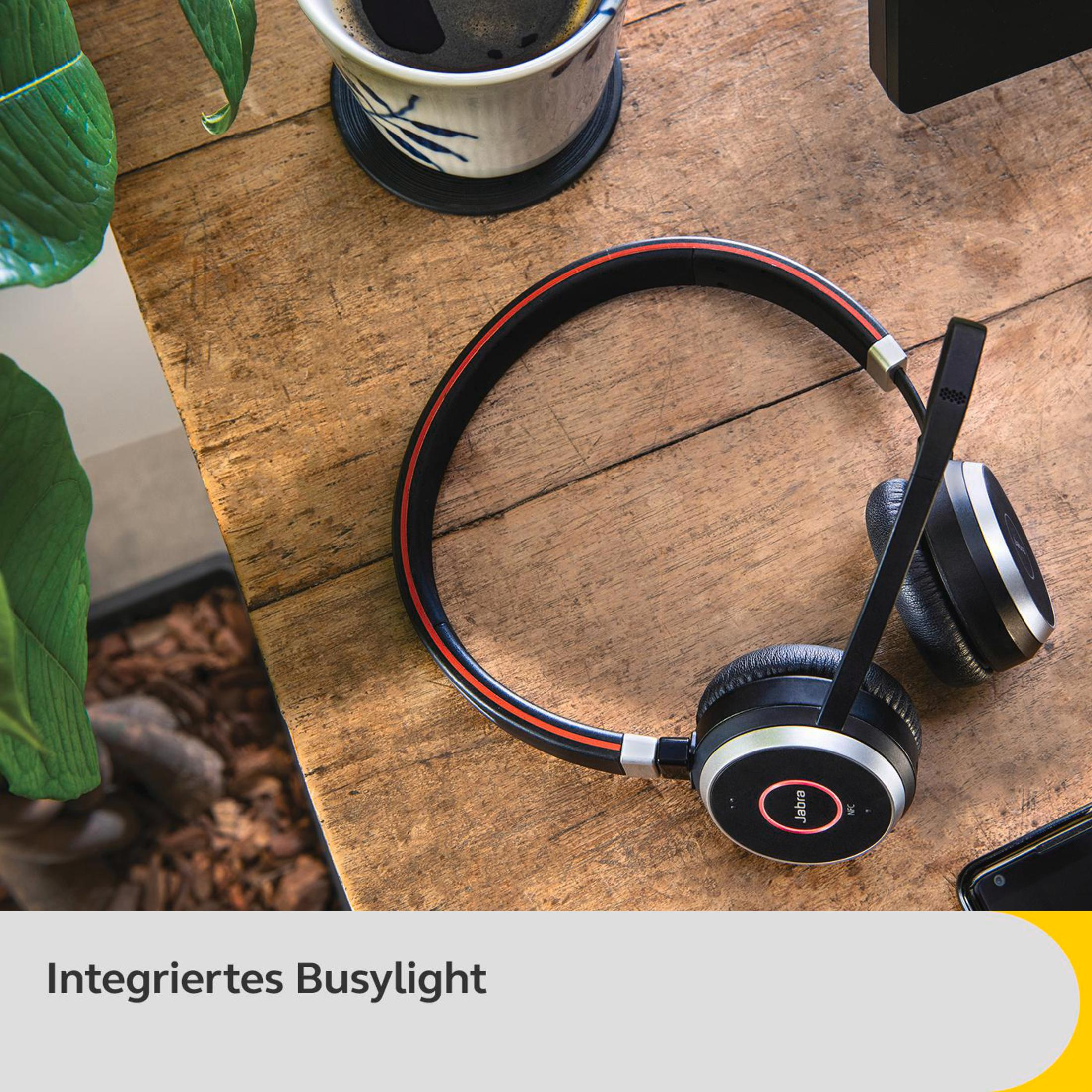 Słuchawki na drewnianym biurku. Czarne i czerwone detale, filiżanka kawy i roślina.