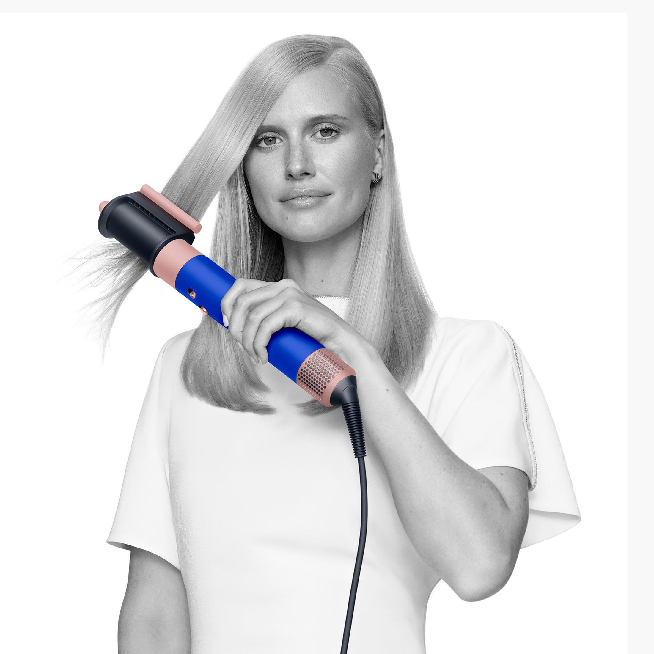 Donna che si acconcia i capelli con un asciugacapelli blu e rosa, sfondo bianco.