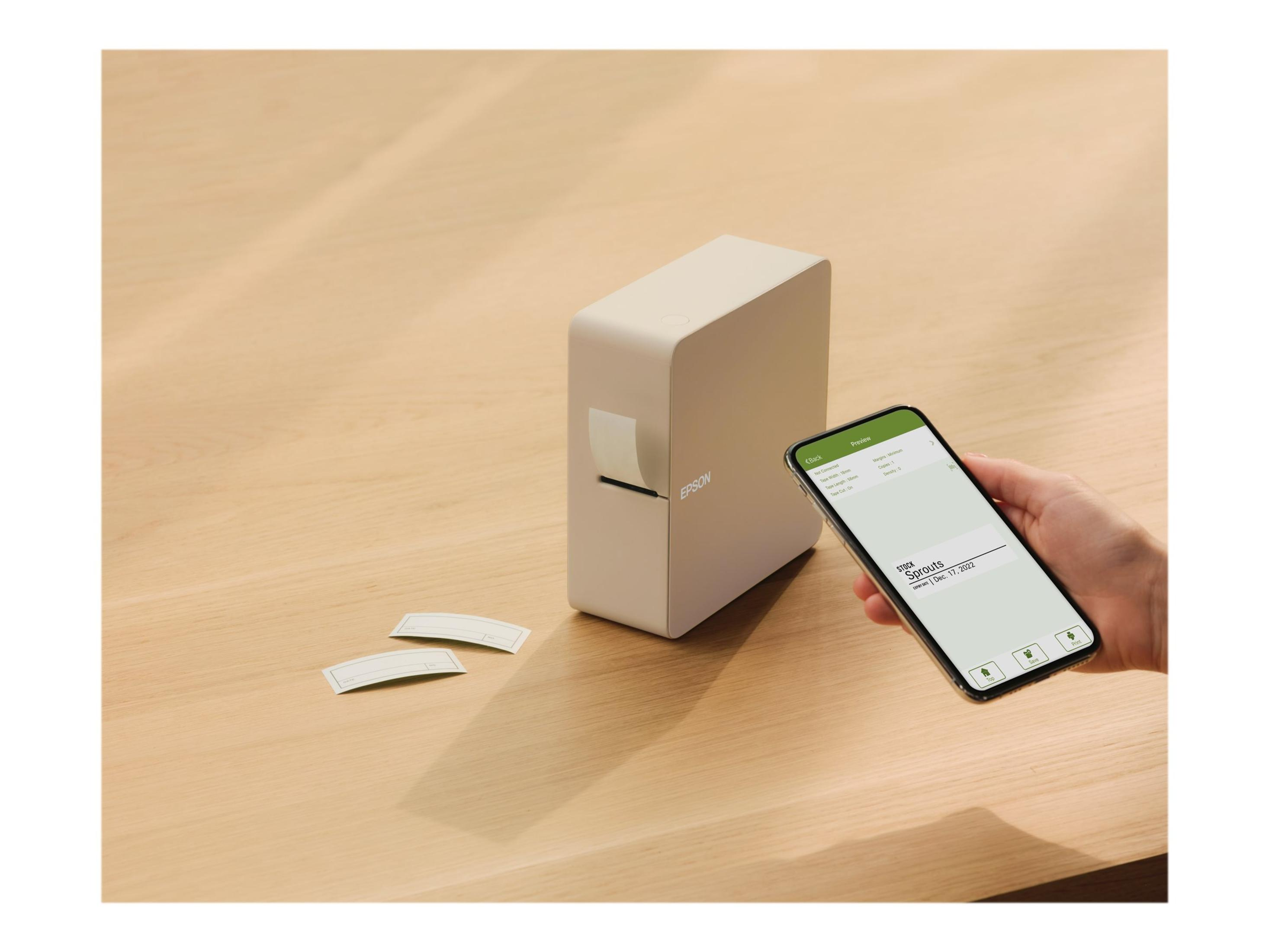 Ein Etikettendrucker und ein Smartphone auf einem Holztisch. Das Telefon zeigt ein Etikettendesign.