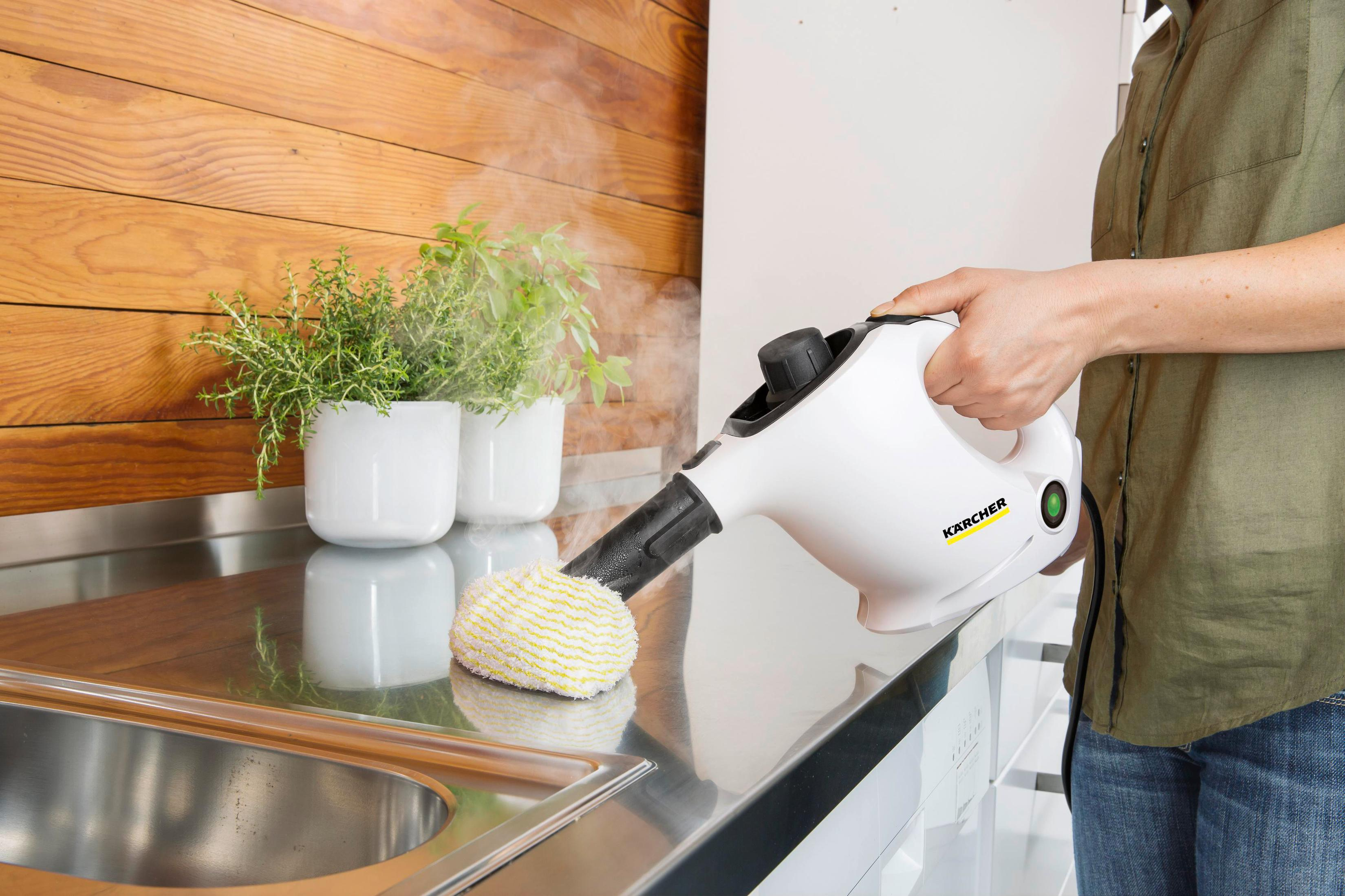 Osoba używa białej myjki parowej na metalowym blacie. Rośliny w tle.