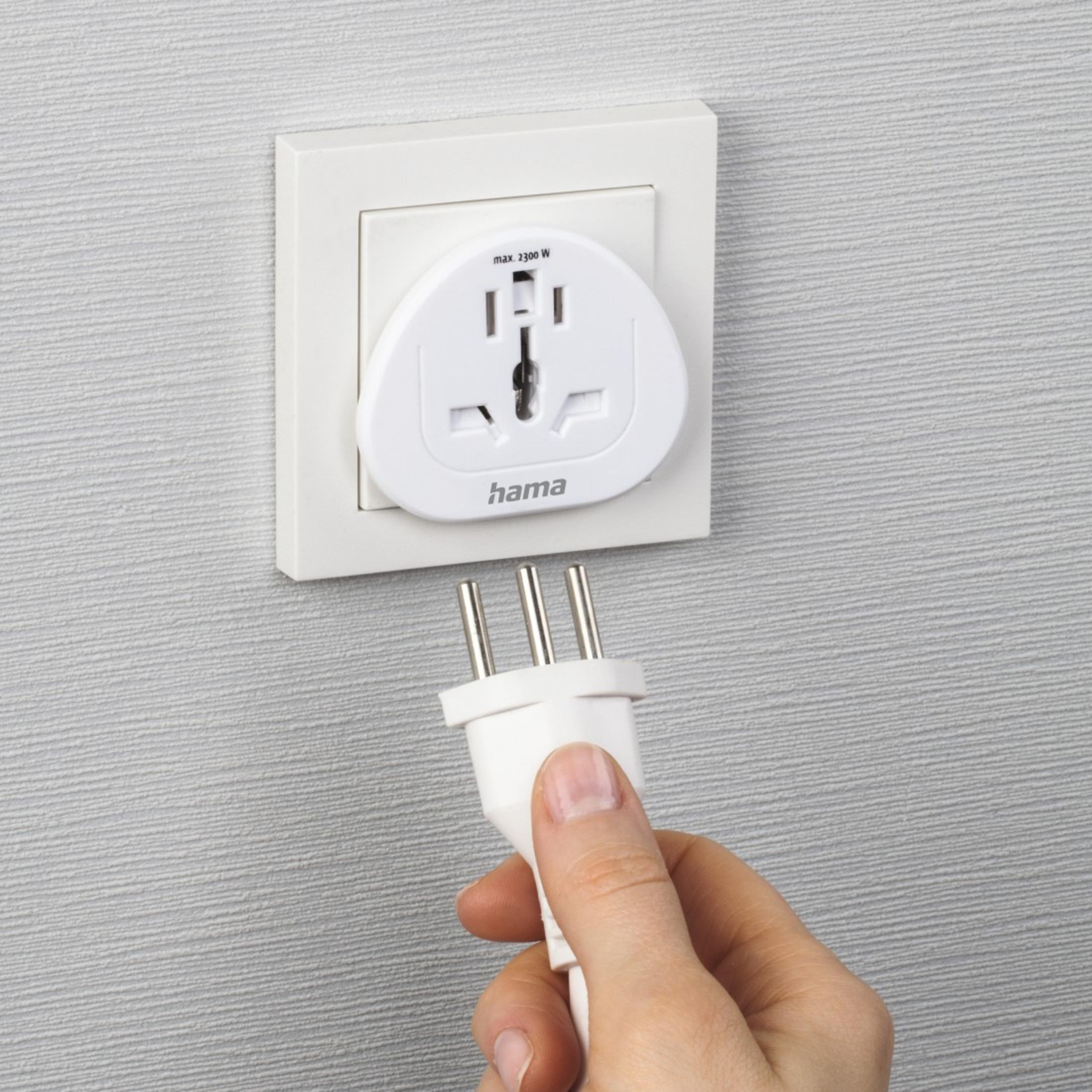Eine Hand hält einen Stecker neben einem Wandadapter mit mehreren Steckplätzen.