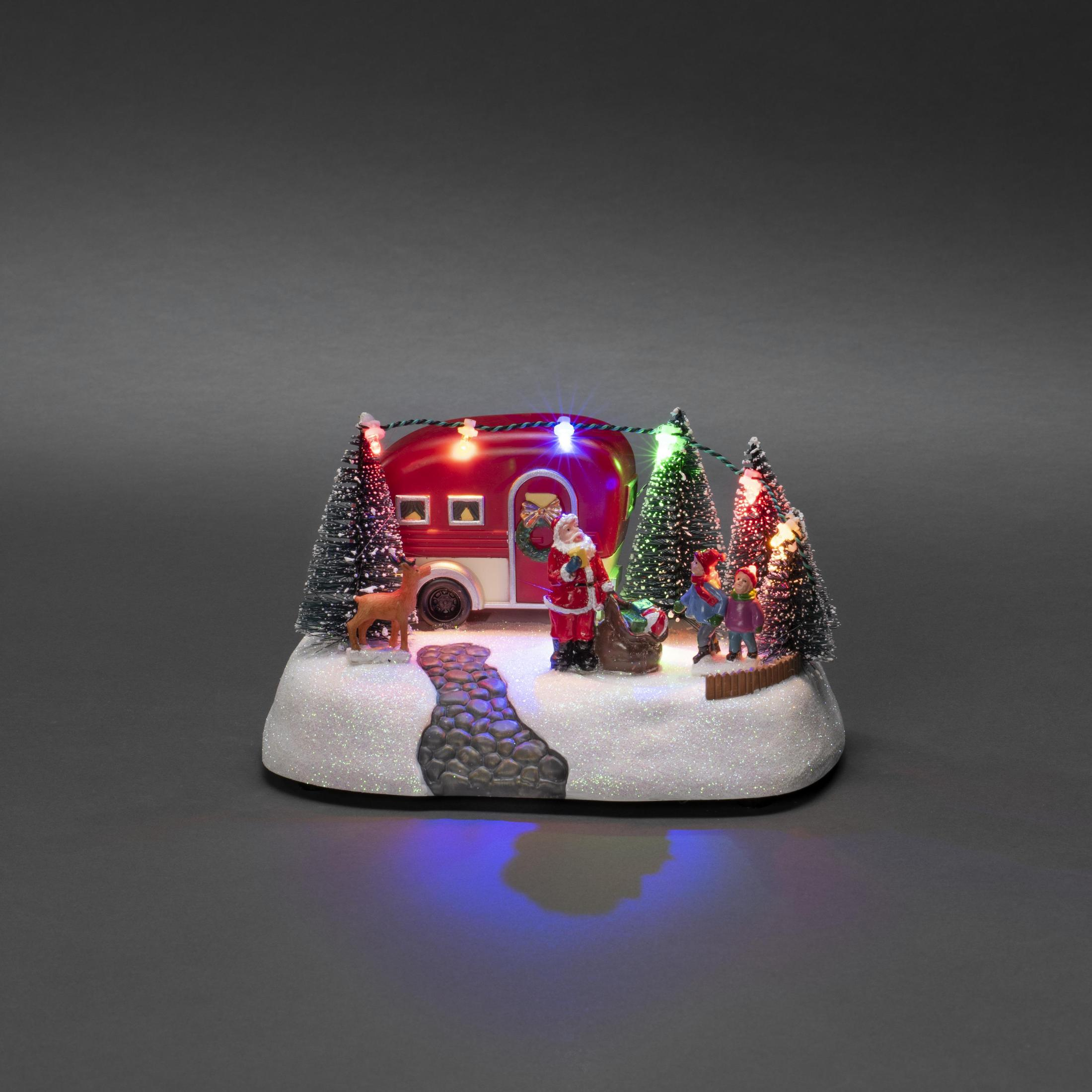 Eine Weihnachtsszene mit einem roten Wohnwagen, Santa und einer verschneiten Landschaft mit Lichtern.