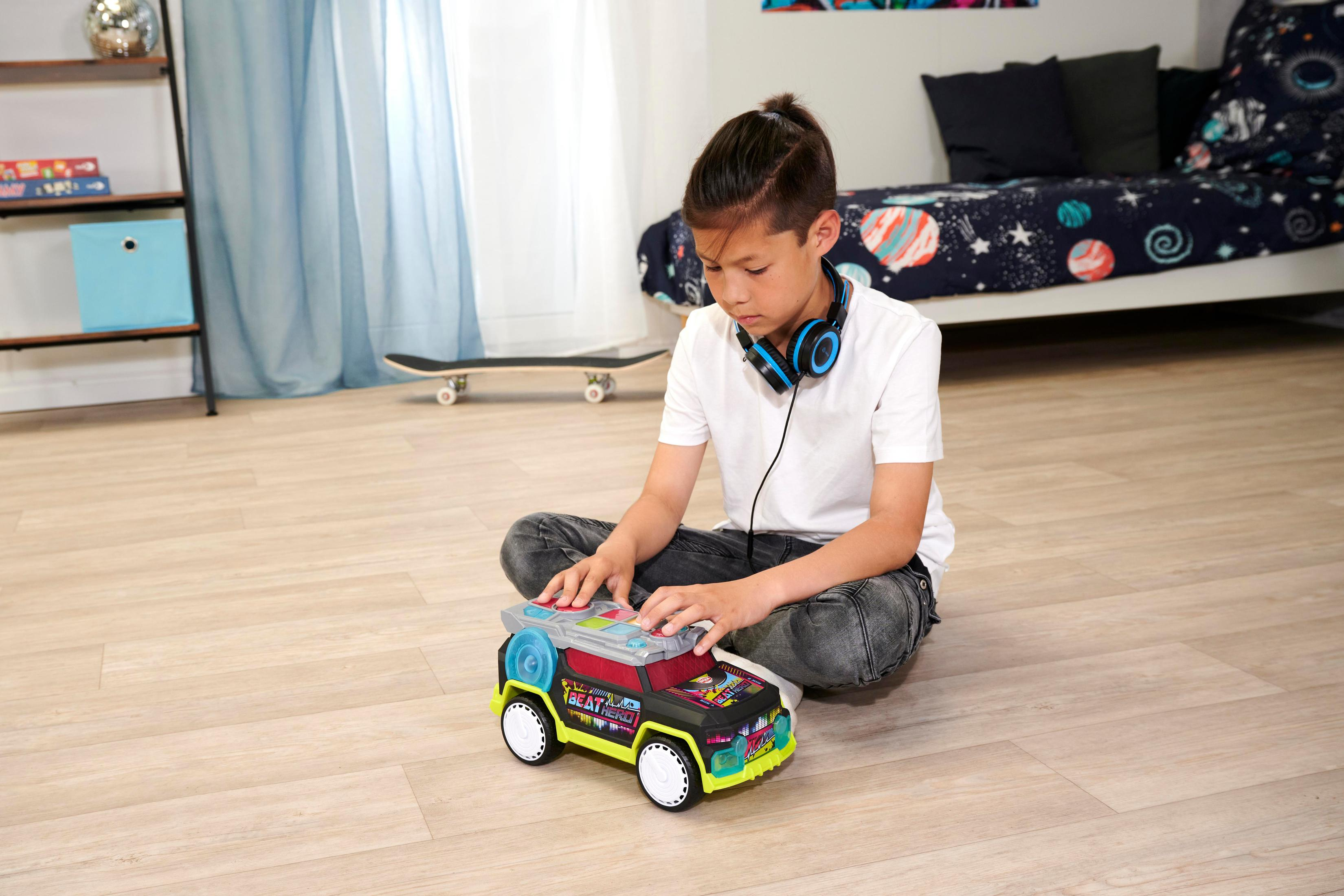 Chłopiec bawi się zabawką na podłodze, w tle deskorolka i łóżko.