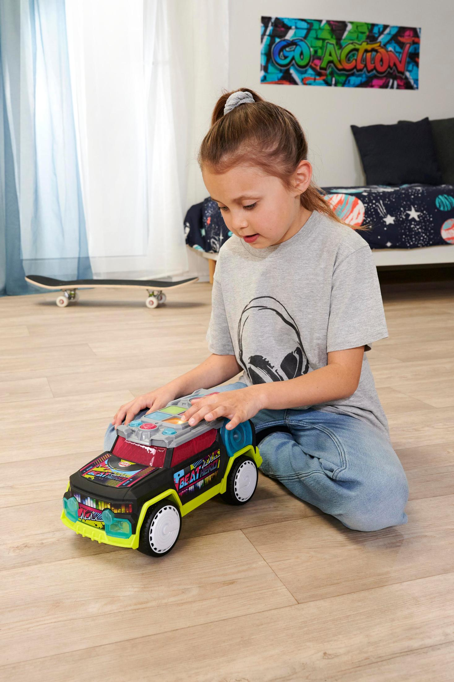 Dziewczynka bawiąca się zabawką-samochodem. Samochód jest kolorowy i ma wzory w stylu graffiti.