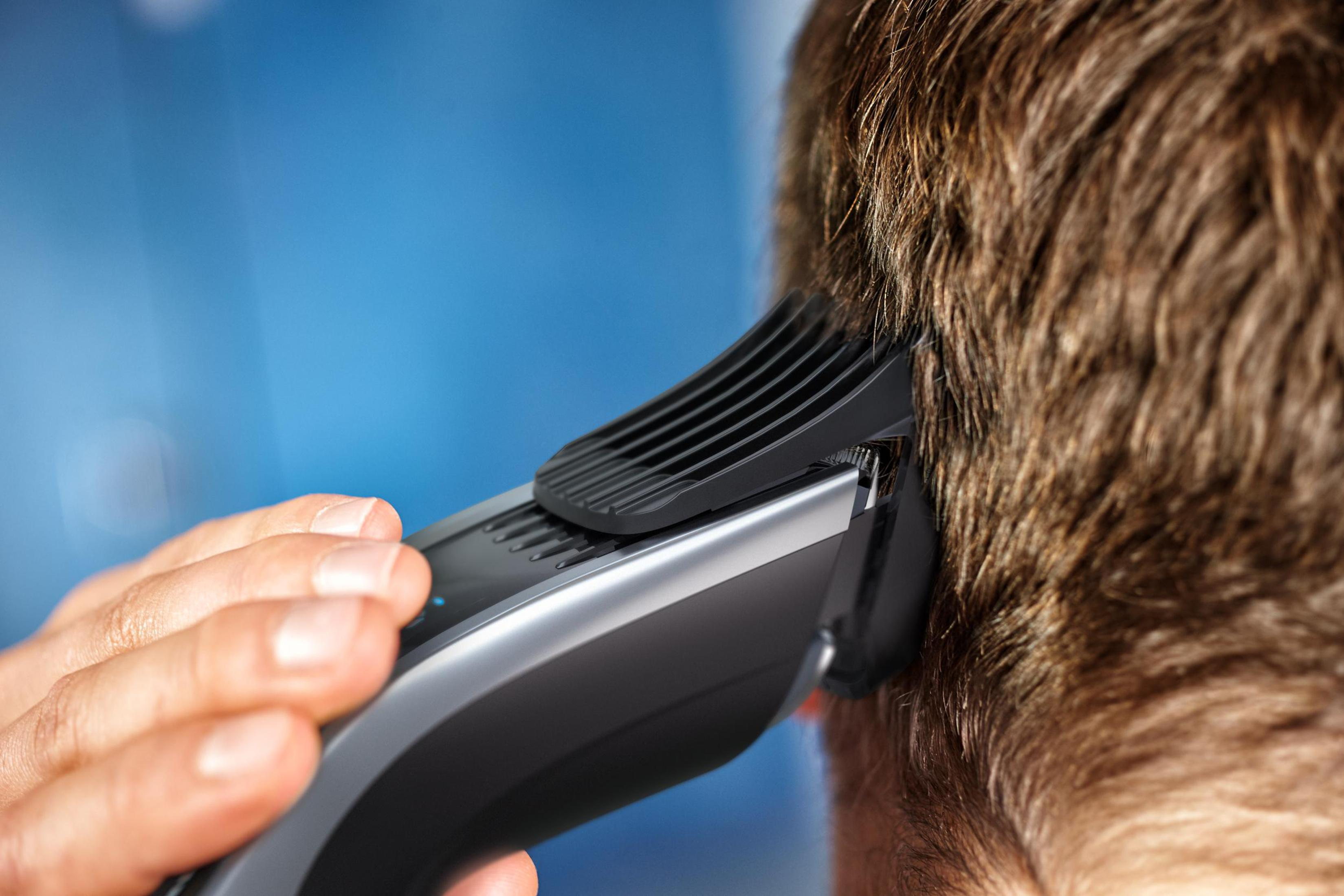 Mano usando una cortadora de pelo negra y gris, cortando cabello cerca de la oreja.