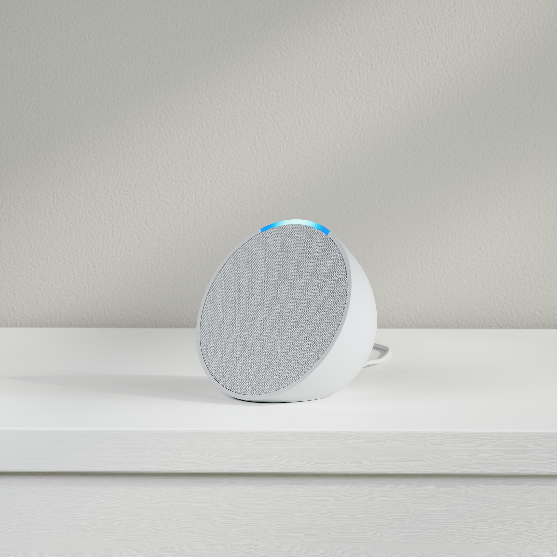 Altavoz Amazon Echo Dot blanco sobre una superficie blanca. Fondo gris claro.