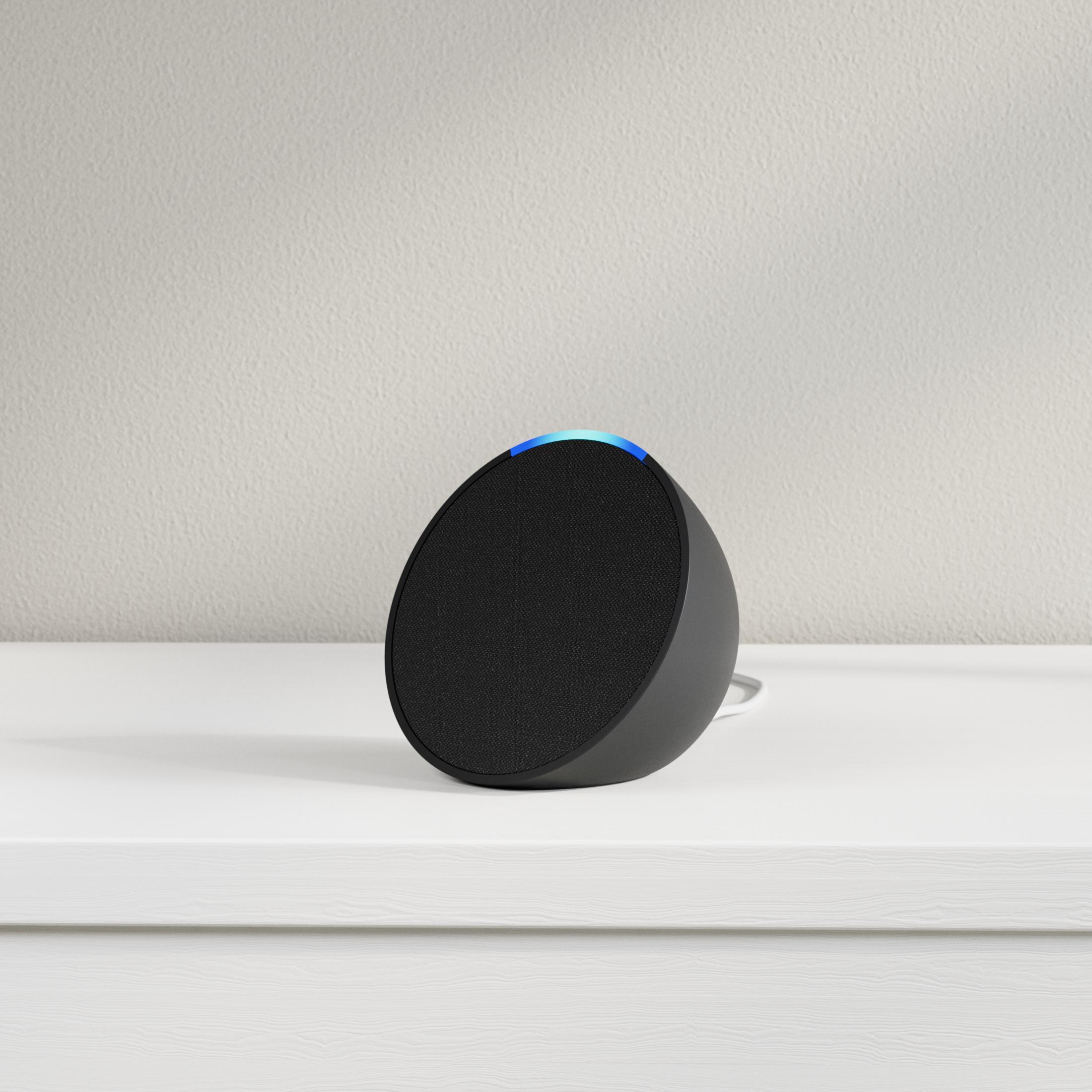 Czarny, sferyczny głośnik inteligentny z niebieskim światłem u góry, na białej powierzchni.