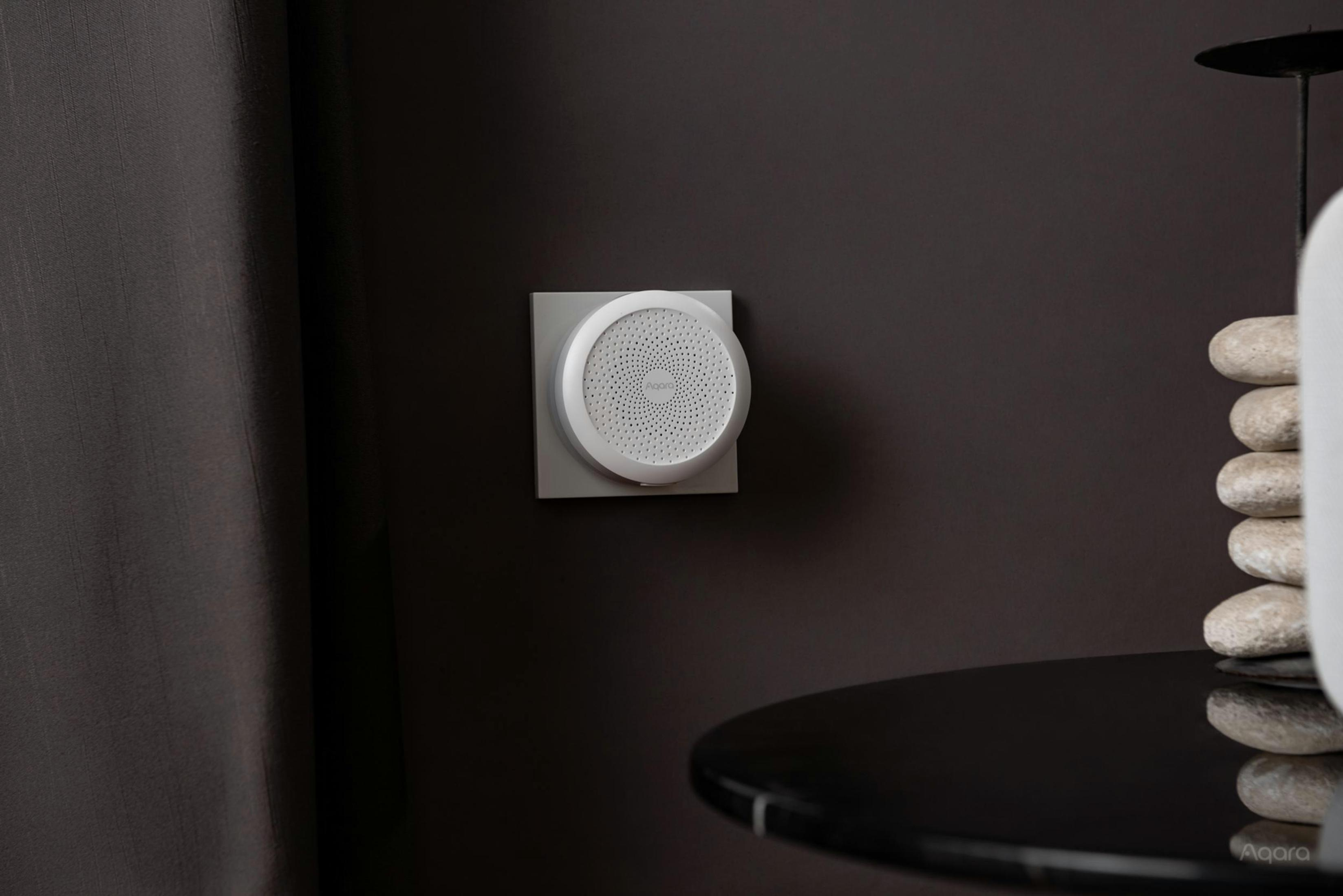 Wit Aqara-apparaat aan een donkere muur. Zwarte tafel en decoratieve items op de voorgrond.