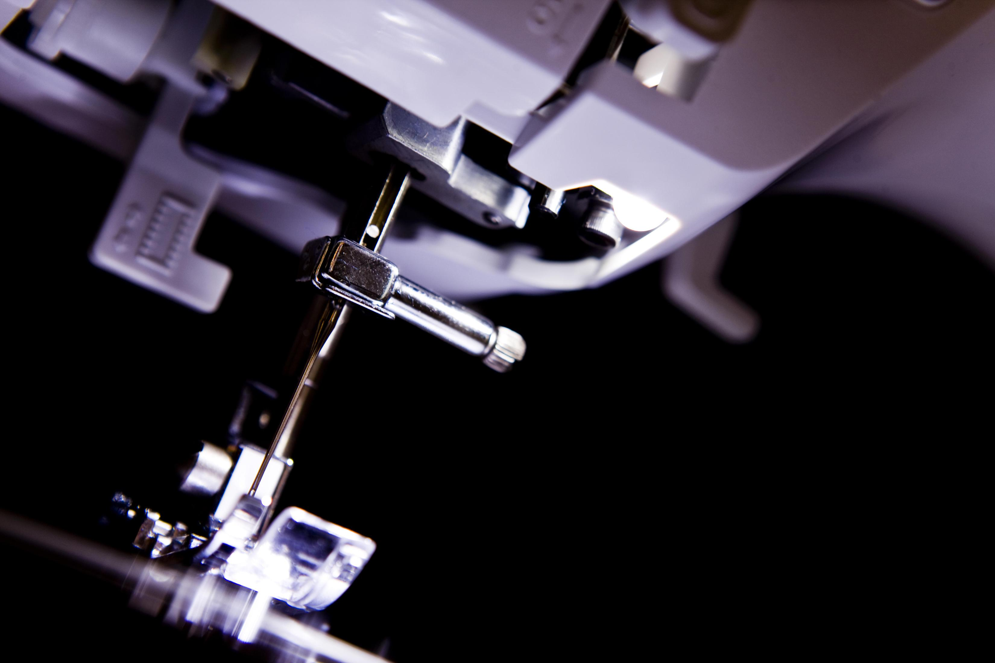 Zbliżenie igły i mechanizmu maszyny do szycia, czarne tło.