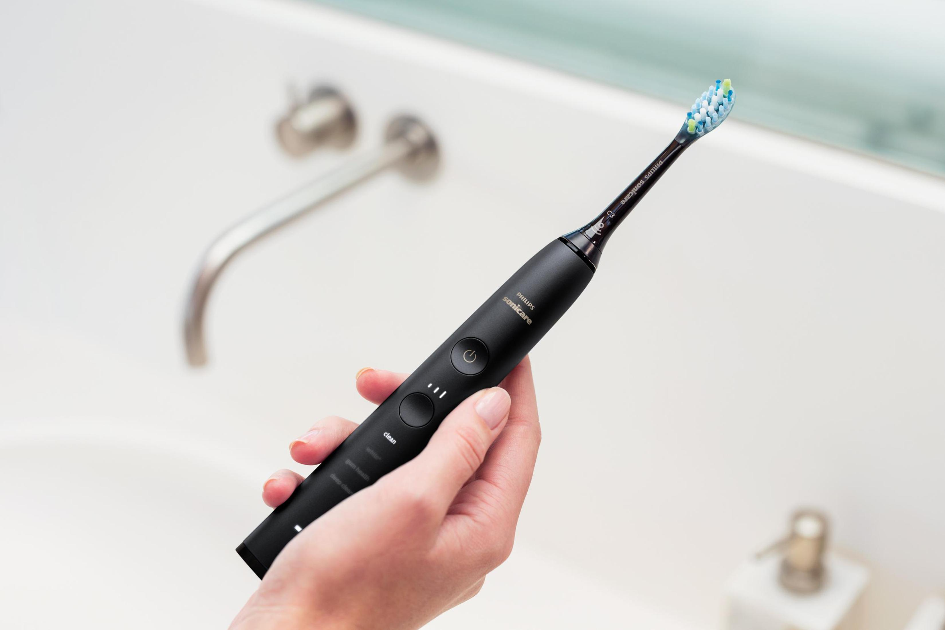 Uno spazzolino elettrico nero tenuto in mano. Il lavandino e il rubinetto sono sullo sfondo.