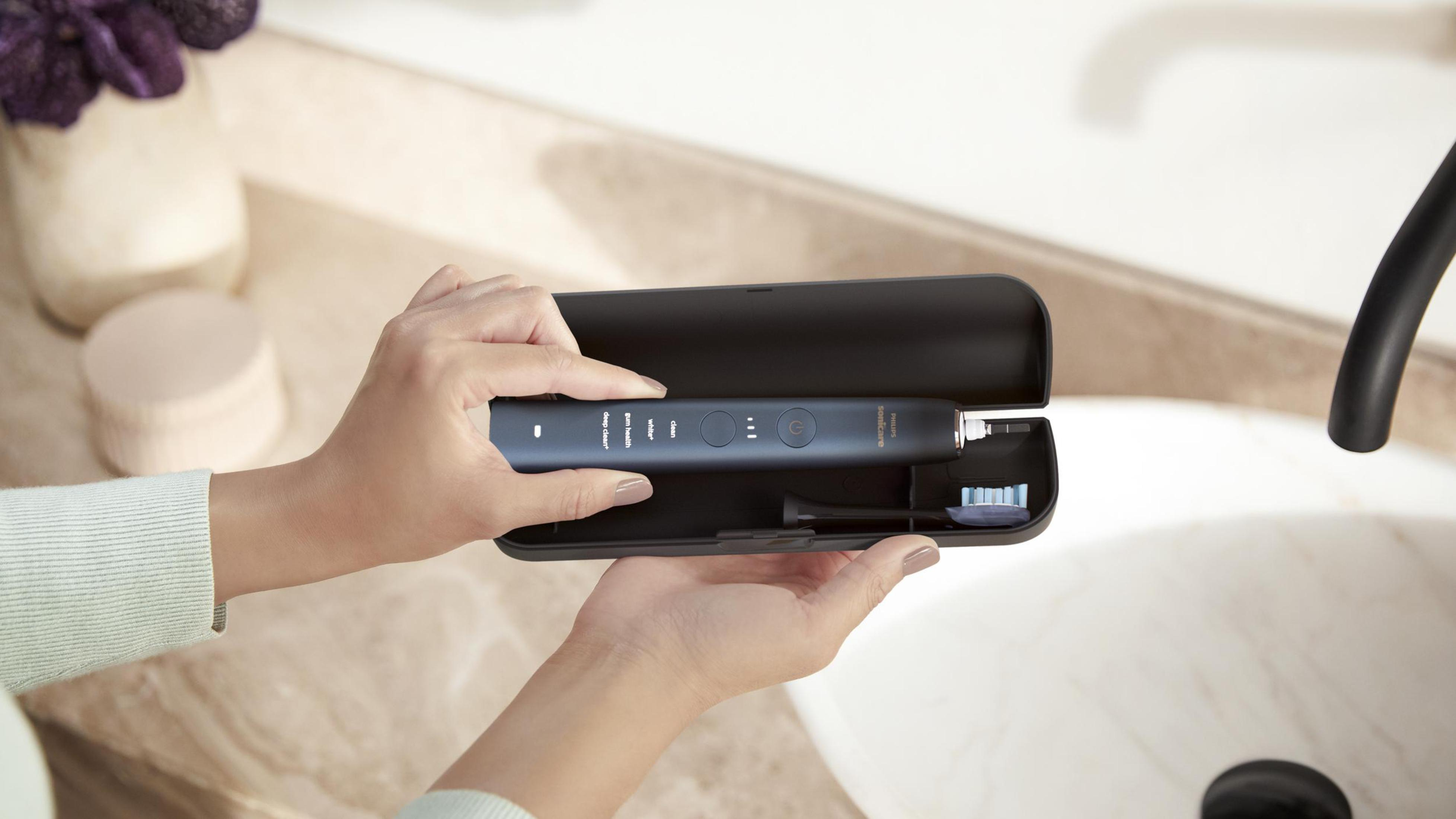 Osoba trzymająca szczoteczkę Philips Sonicare i etui nad umywalką.