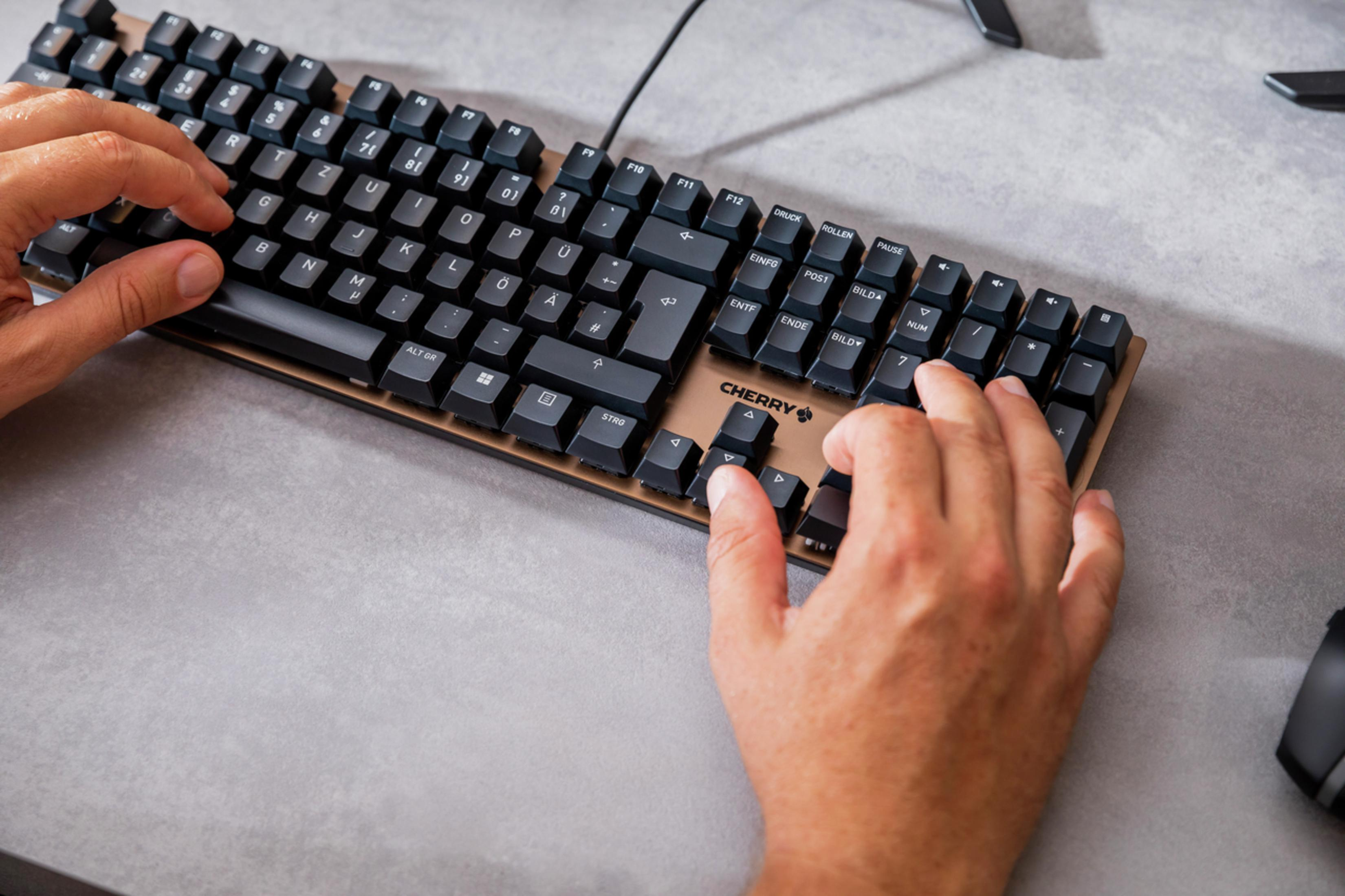Hände tippen auf einer Cherry-Tastatur. Die Tastatur ist schwarz mit Holzrahmen.
