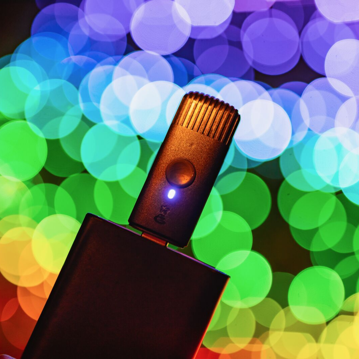 Czarne urządzenie z niebieskim światłem na górze, obok czarnego pudełka. Kolorowe tło bokeh.