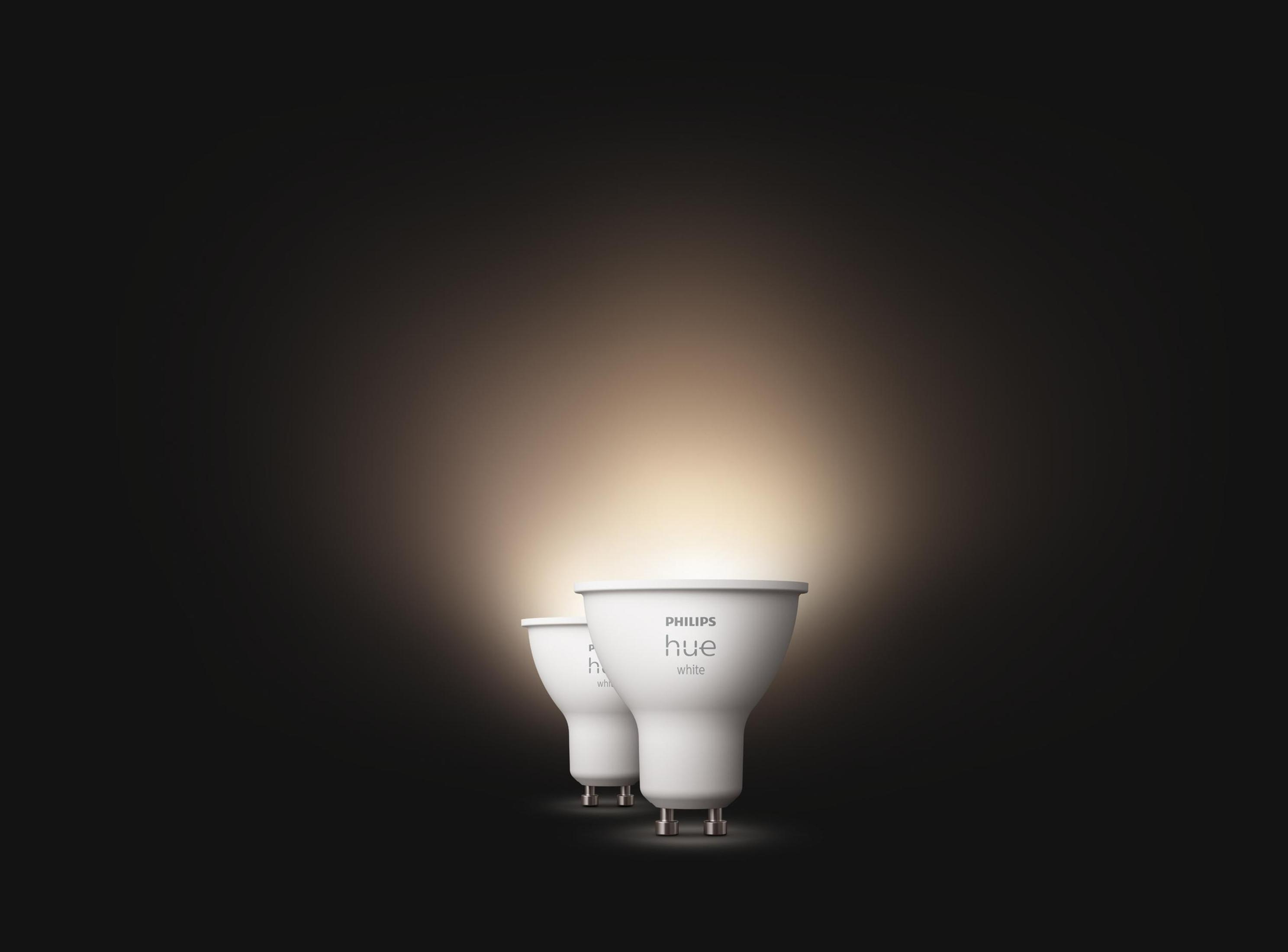 Dwie białe żarówki LED Philips Hue świecą jasnym światłem na ciemnym tle.