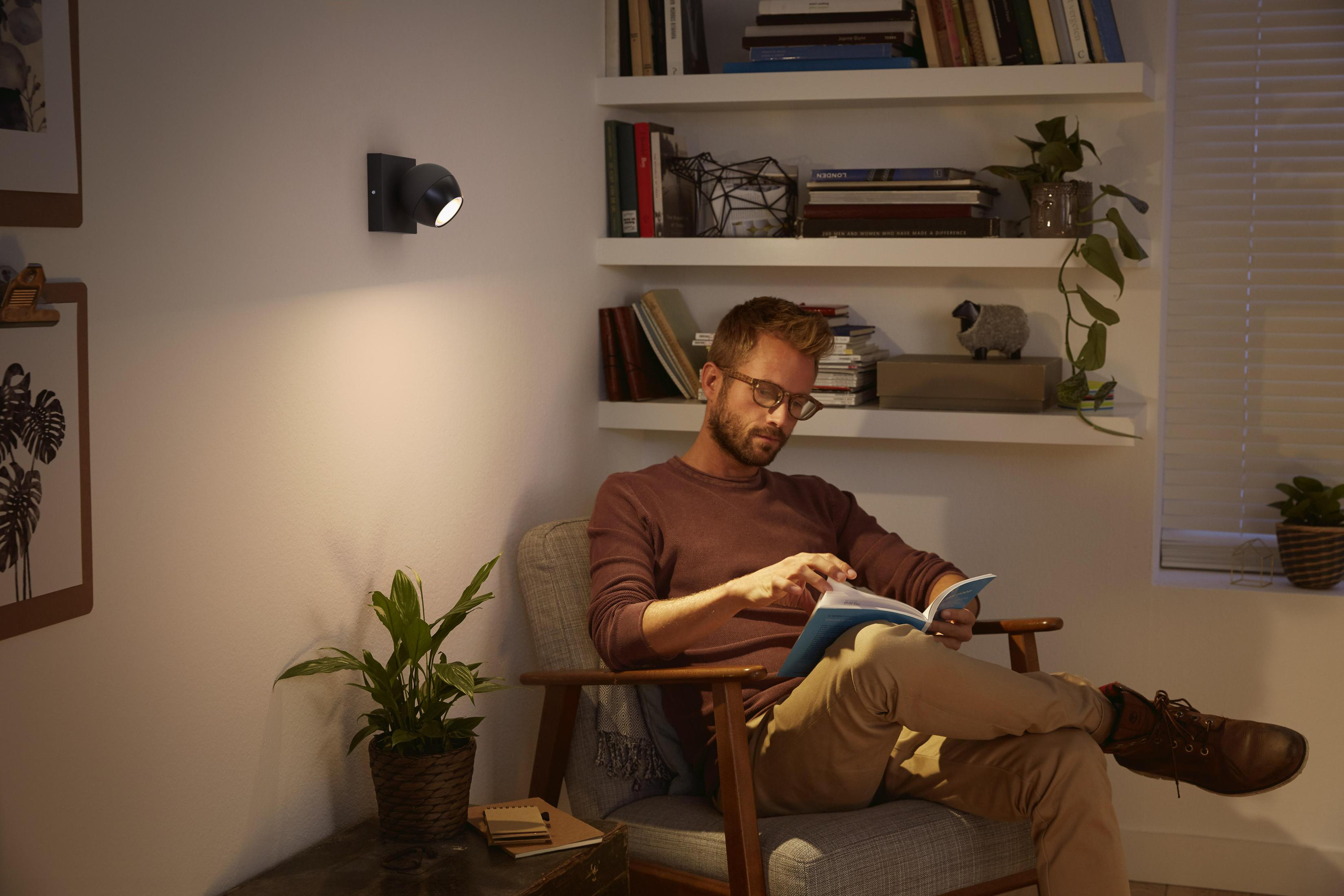 Un uomo legge un libro in una stanza illuminata da un'applique e una lampada.