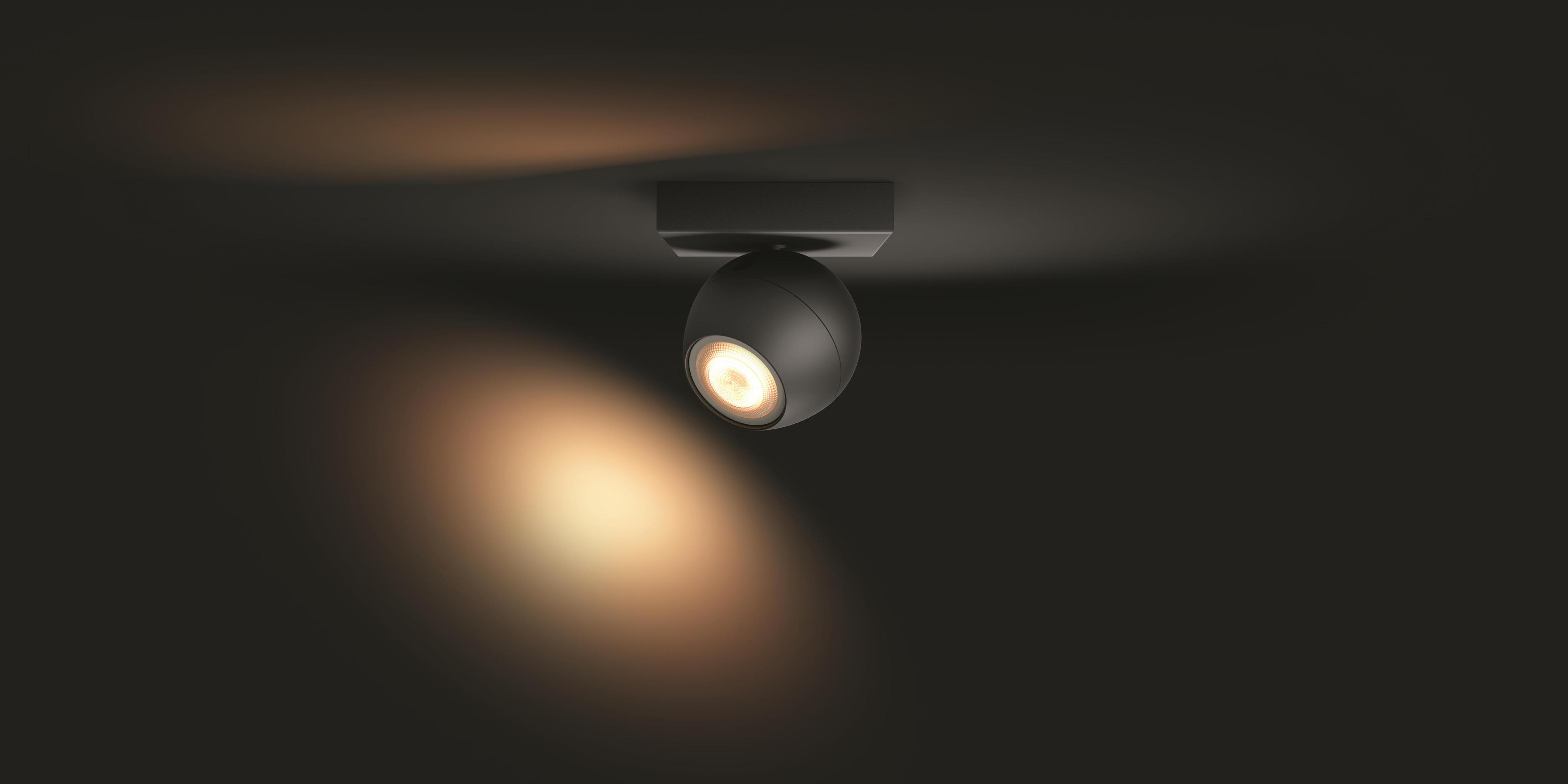 Un faretto nero, sferico, è montato su un soffitto. Emette una luce calda verso il basso.