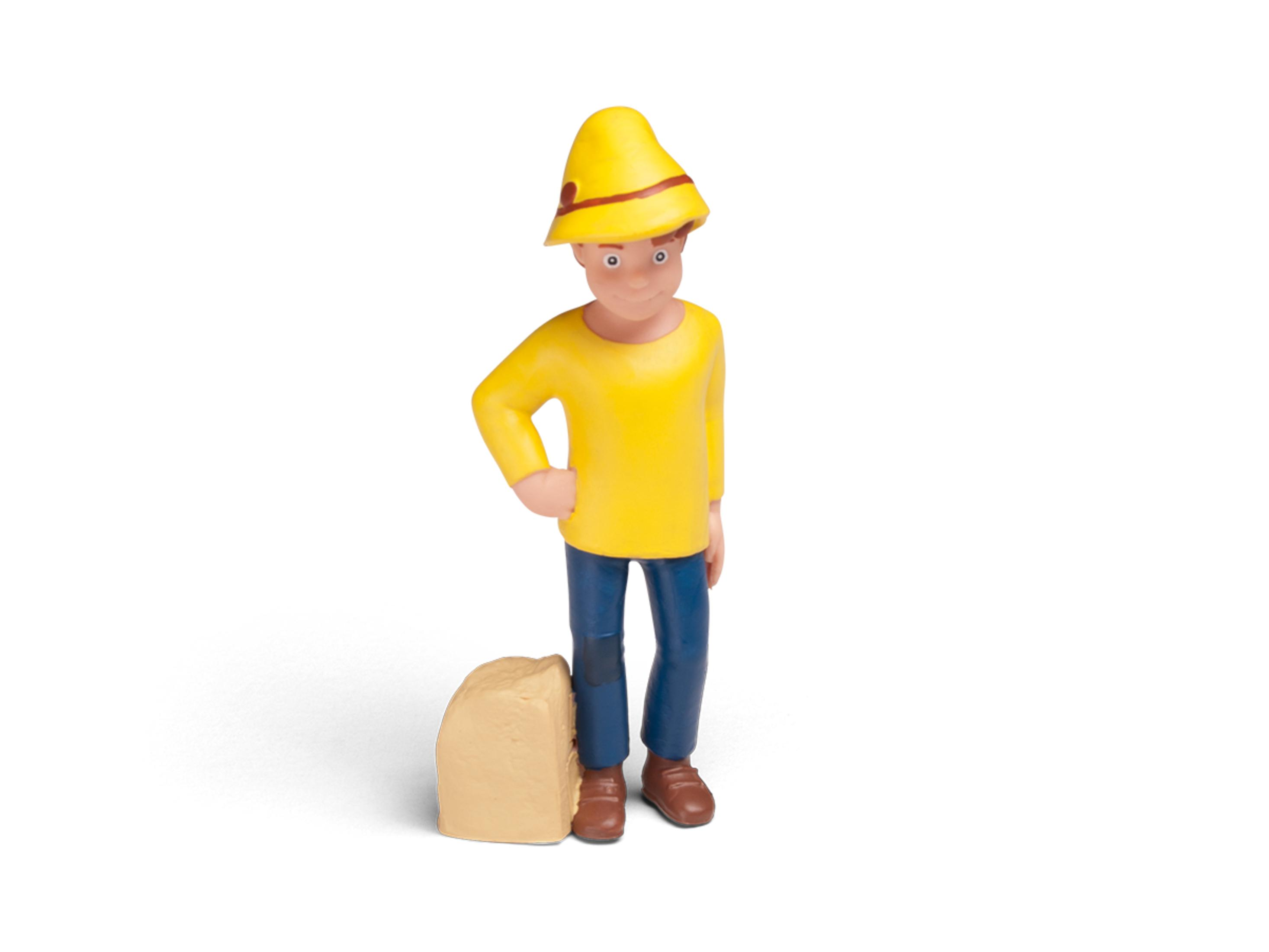 Heidi-Spielfigur, trägt einen gelben Hut und ein Hemd, blaue Hose, steht neben einem Stein.