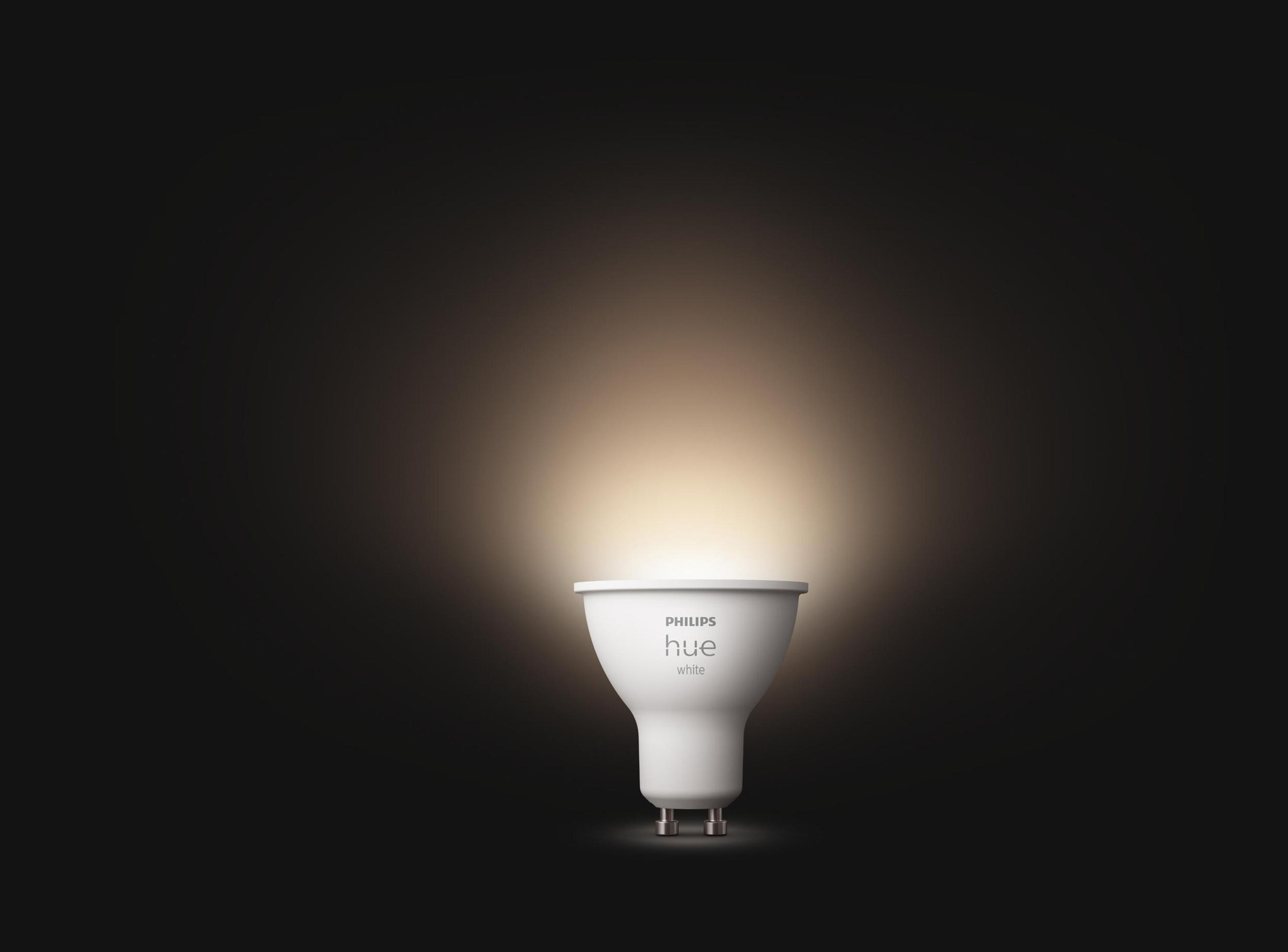 Une ampoule Philips Hue blanche émettant une lueur chaude, sur fond sombre.