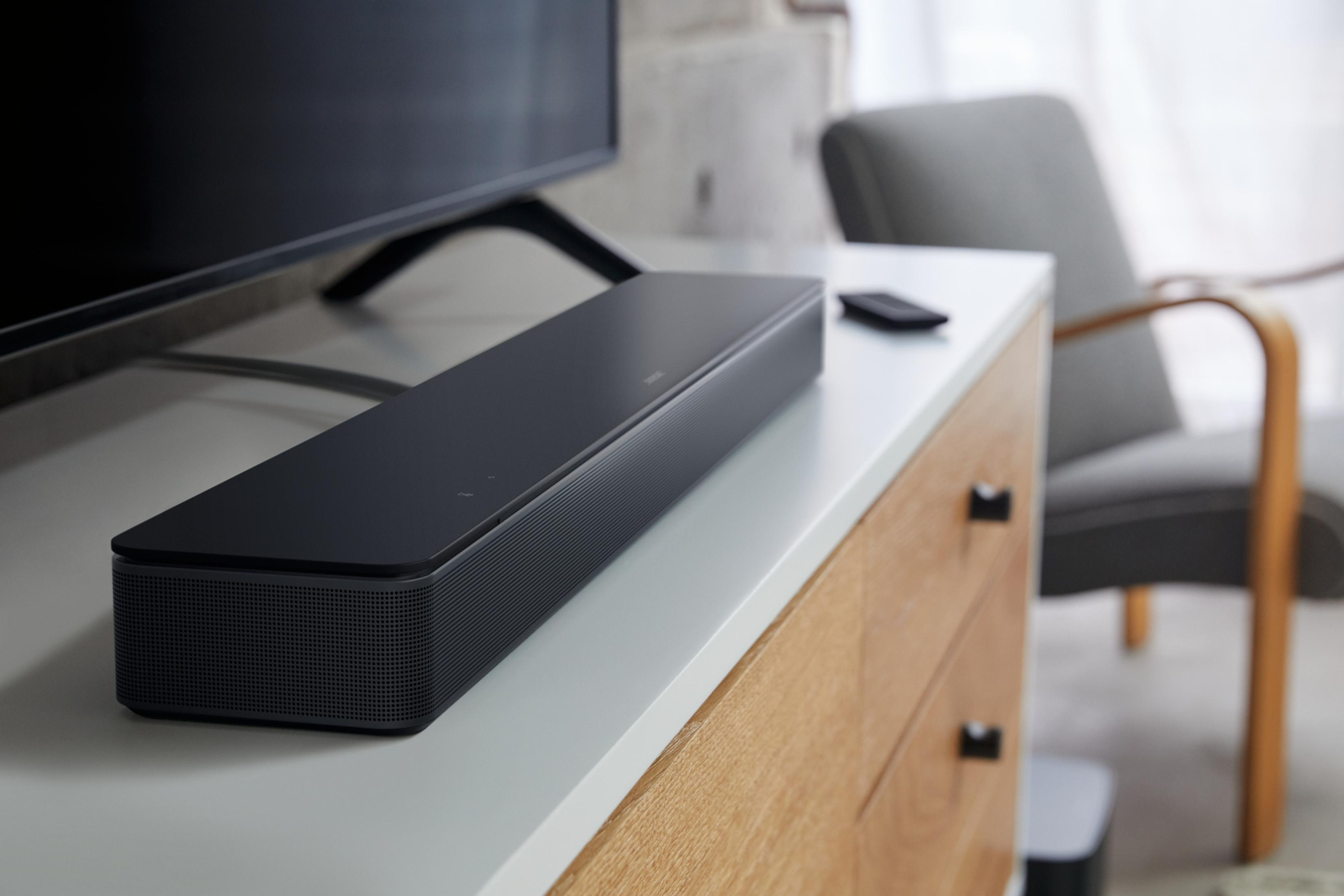 Eine schwarze Soundbar auf einer weißen Kommode. Eine schwarze Fernbedienung liegt obenauf.