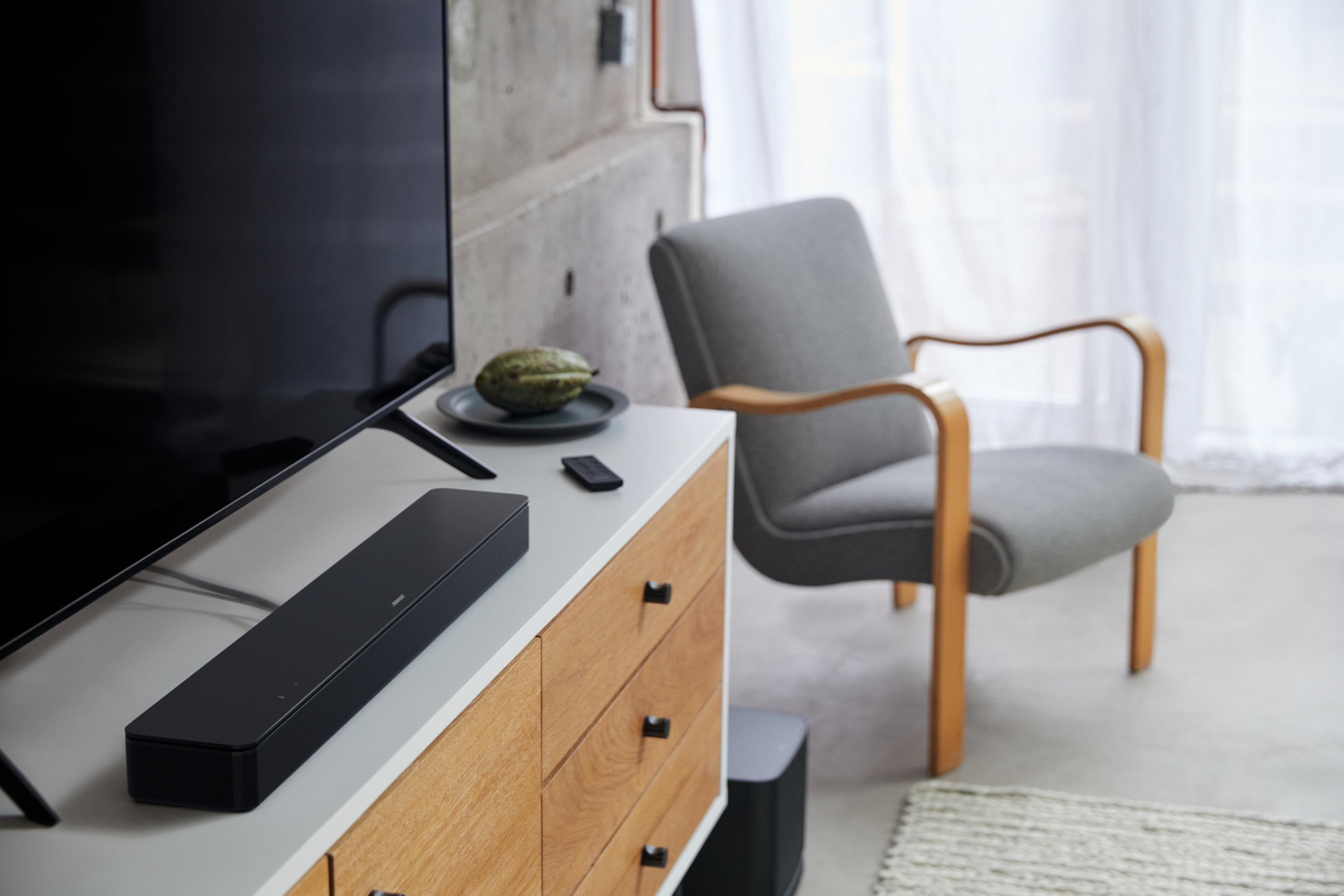 Eine schwarze Soundbar auf einem weißen Schrank, mit TV, Stuhl und Raumdetails.
