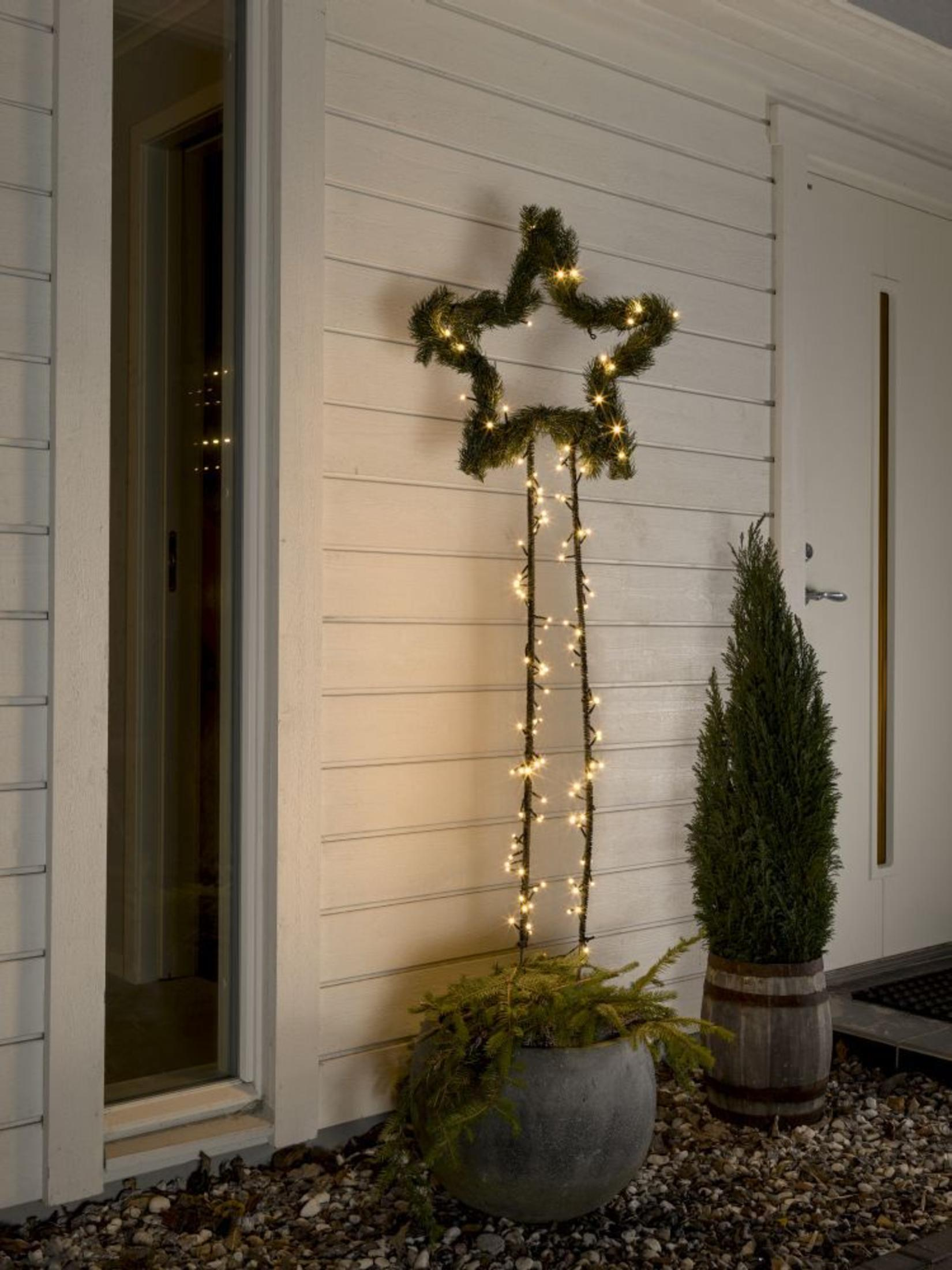 Weihnachtsstern-Dekoration im Freien mit Lichtern, neben einem kleinen Baum.
