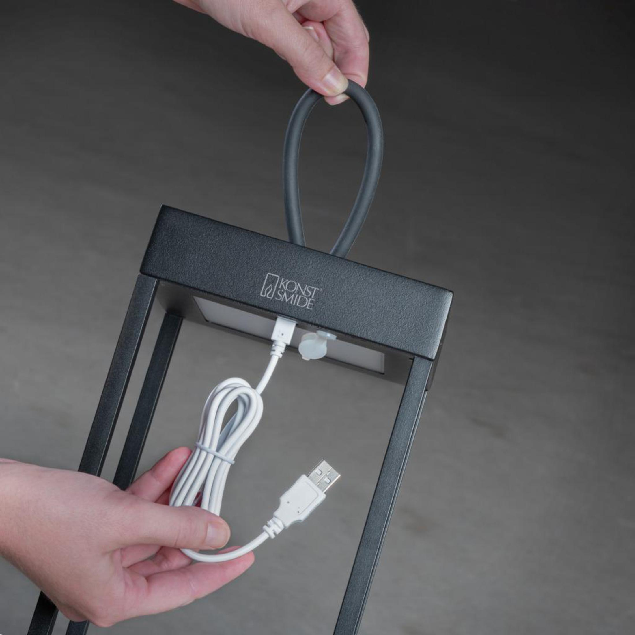 Eine schwarze Laterne wird von Händen gehalten. Ein USB-Kabel ist angeschlossen.