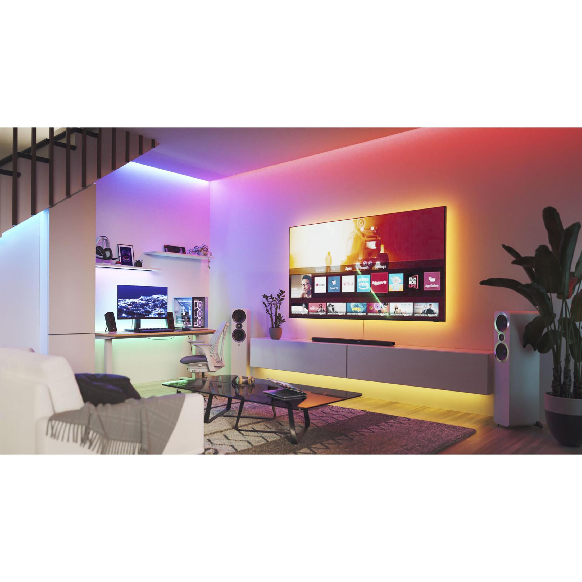 Soggiorno con grande TV, computer, altoparlanti e piante, con luce ambientale colorata.