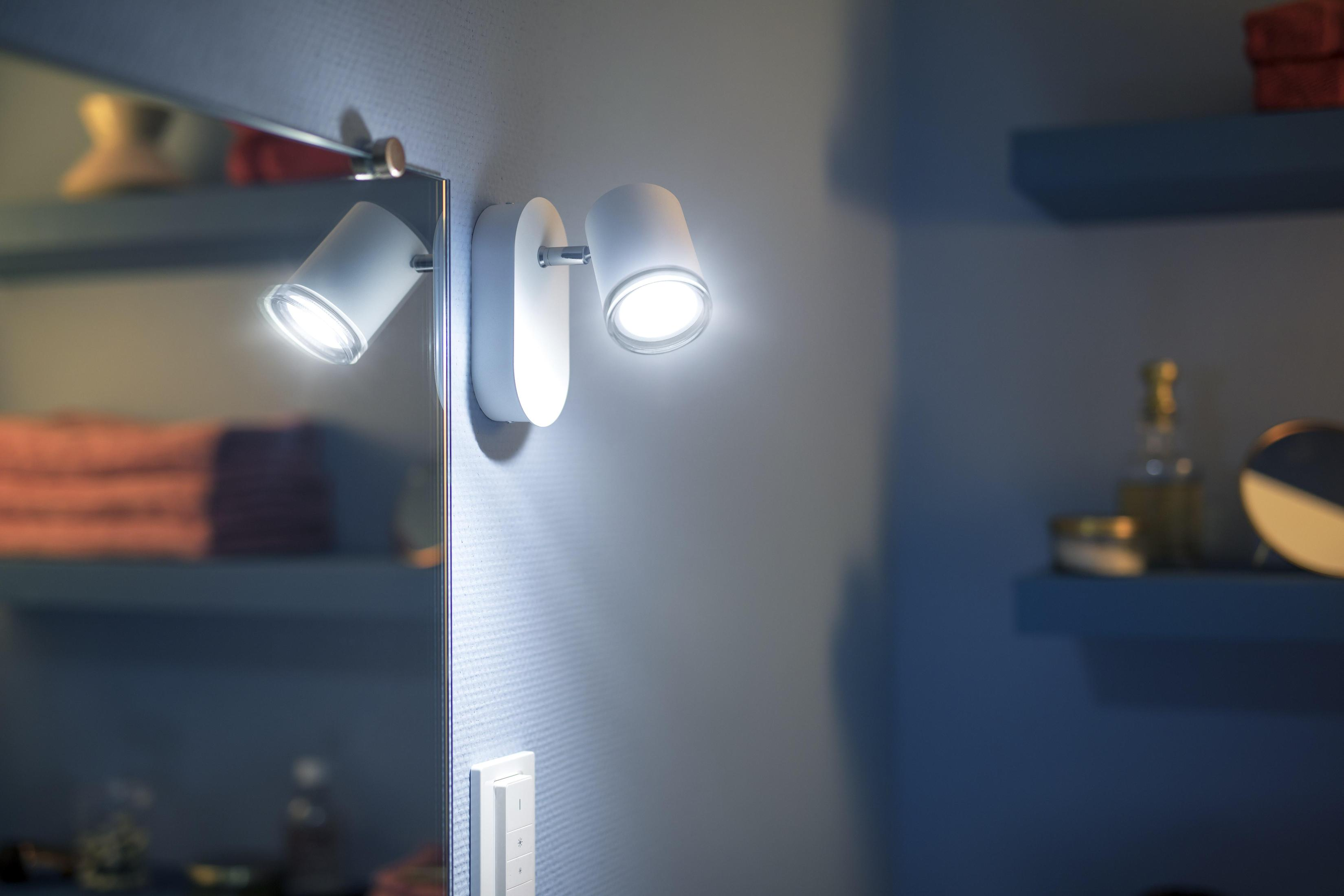 Dos focos blancos montados en una pared junto a un espejo, iluminados.