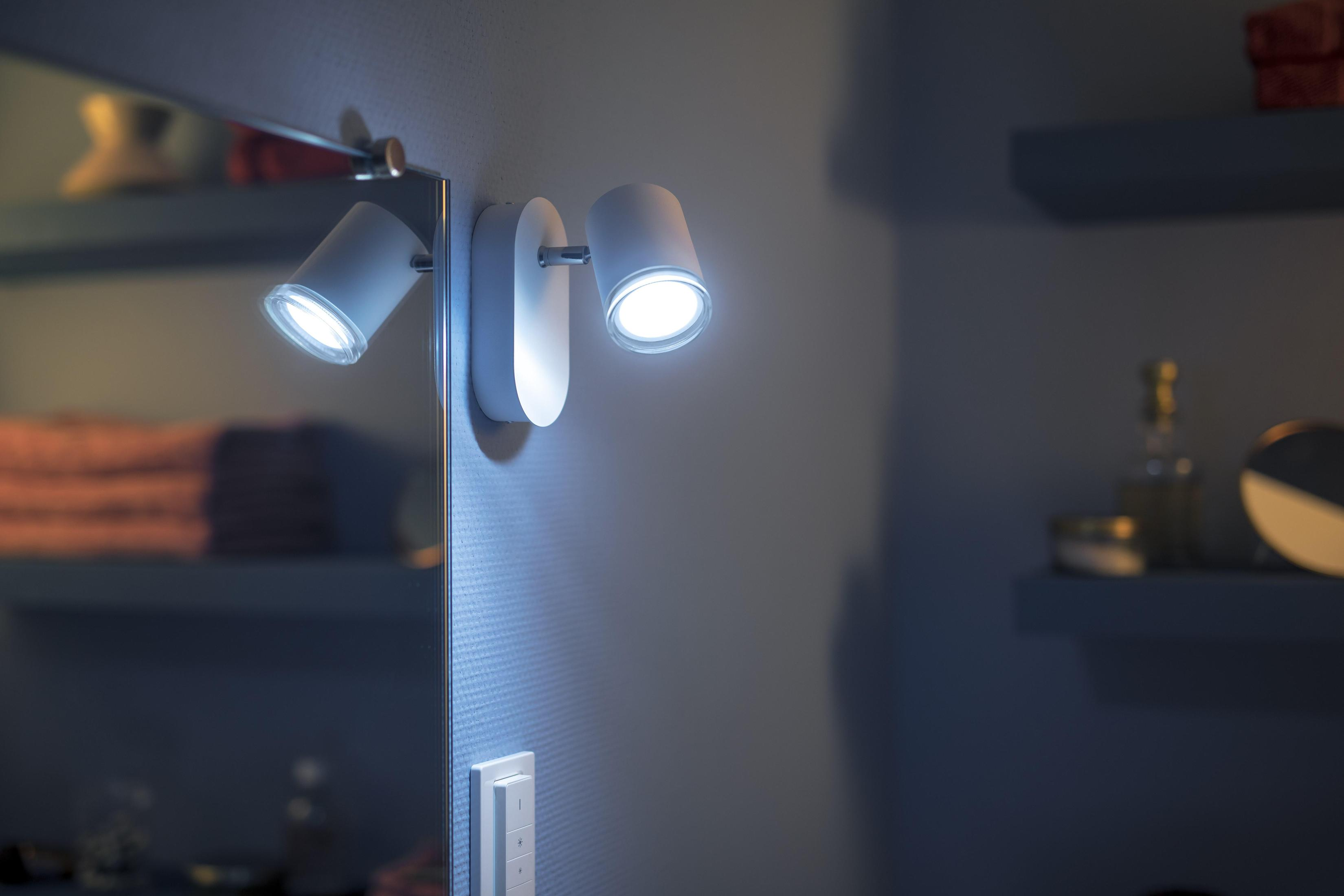 Dos focos blancos modernos en una pared, iluminando un espejo.