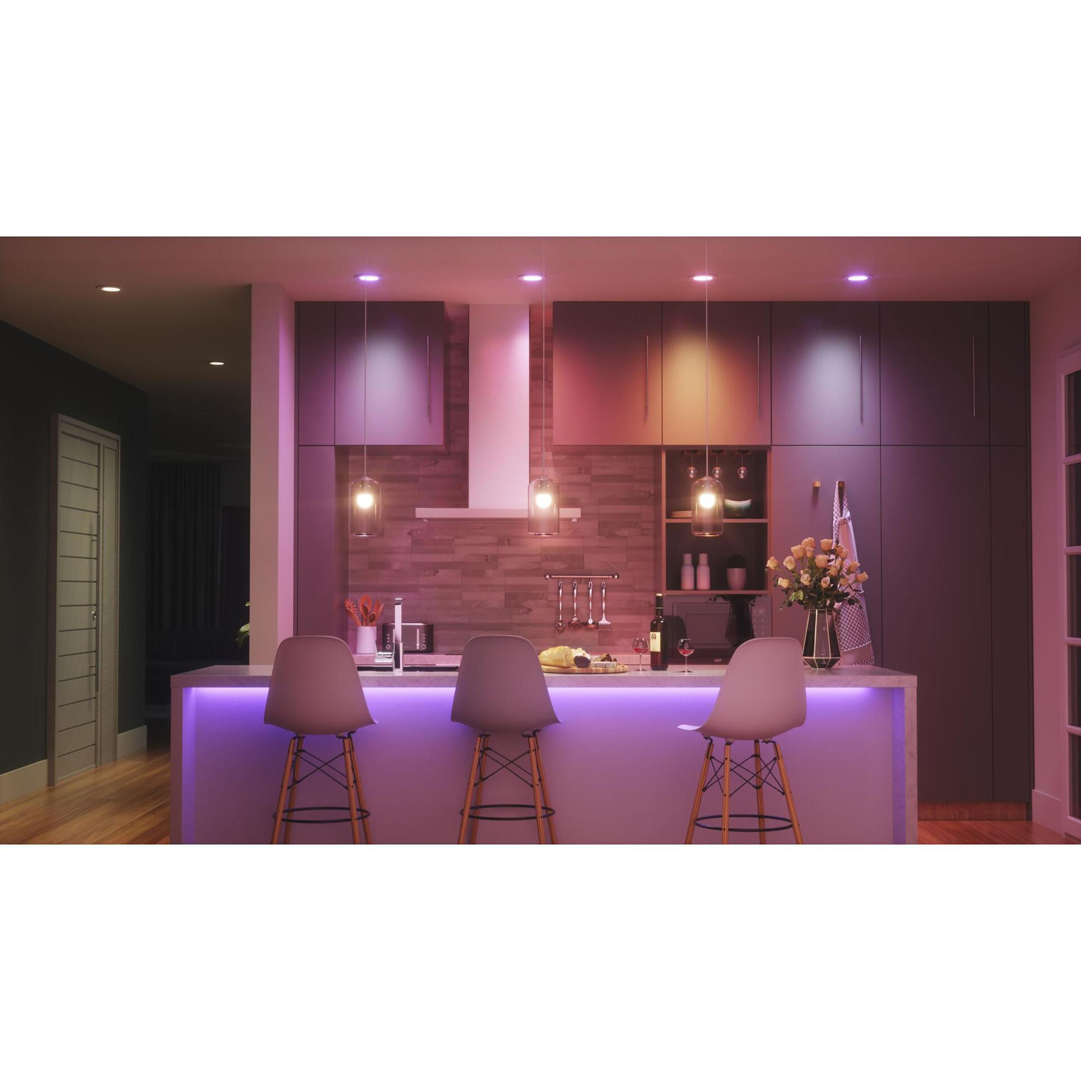 Una cucina moderna con luci viola sull'isola. Sono visibili tre sgabelli, lampade e una bottiglia di vino.