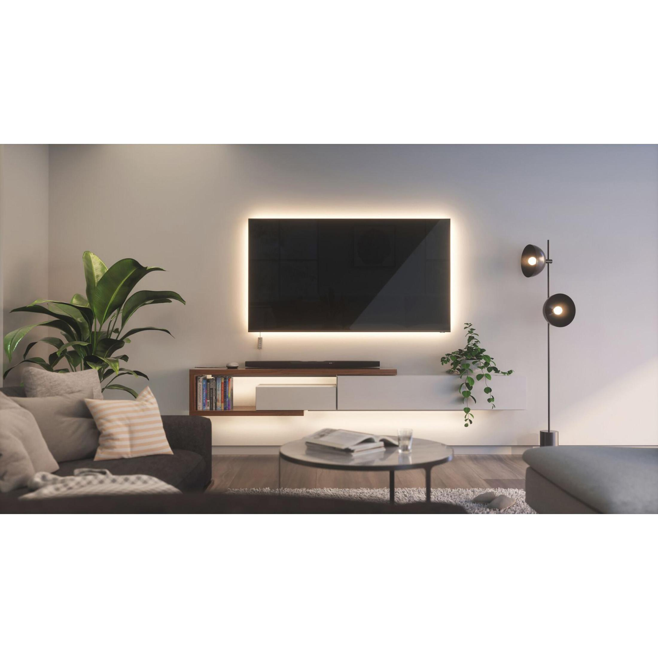 Soggiorno con TV, piante e lampada, divano scuro e tavolino rotondo.