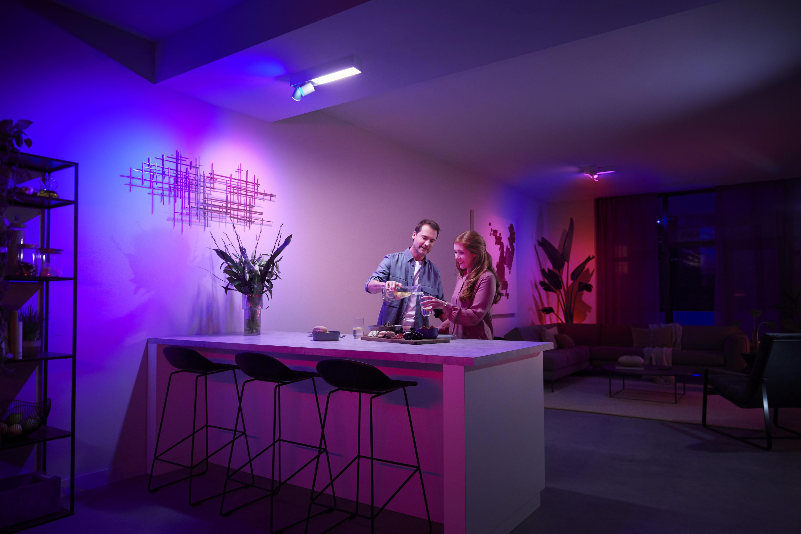 Un couple dans une pièce moderne avec un éclairage coloré. Ils versent une boisson.