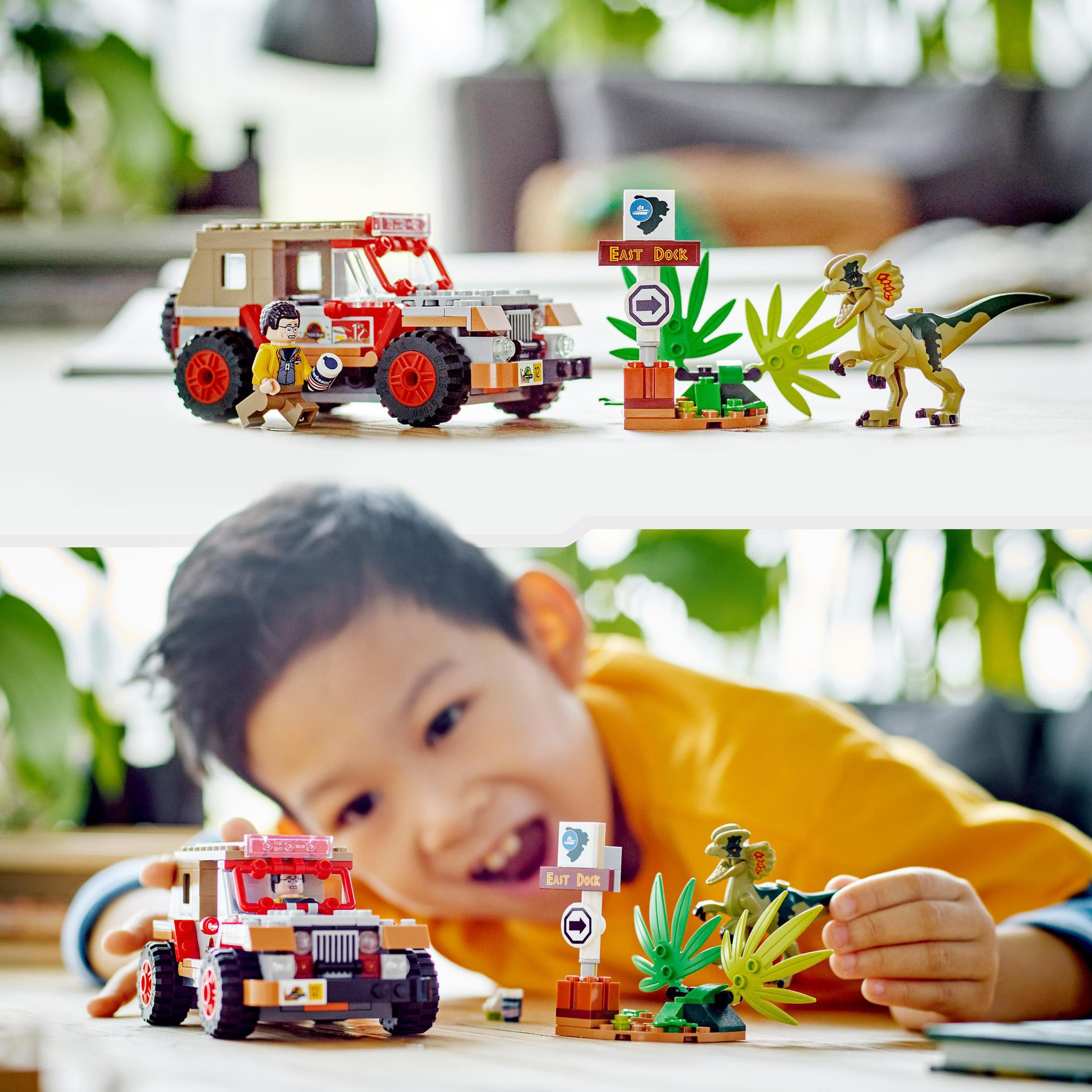 Ein Junge spielt mit einem Lego Jurassic Park Set. Ein Auto, Dinosaurier und Schilder sind sichtbar.