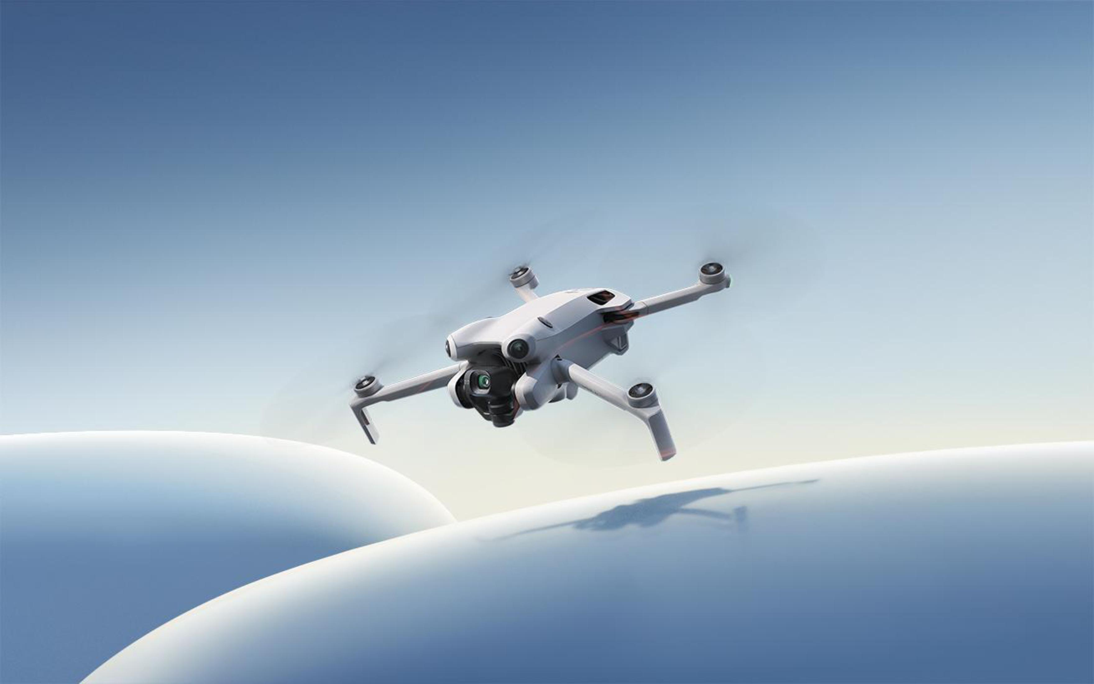 Biały dron w locie nad stylizowanymi niebieskimi wzgórzami na tle niebieskiego nieba.