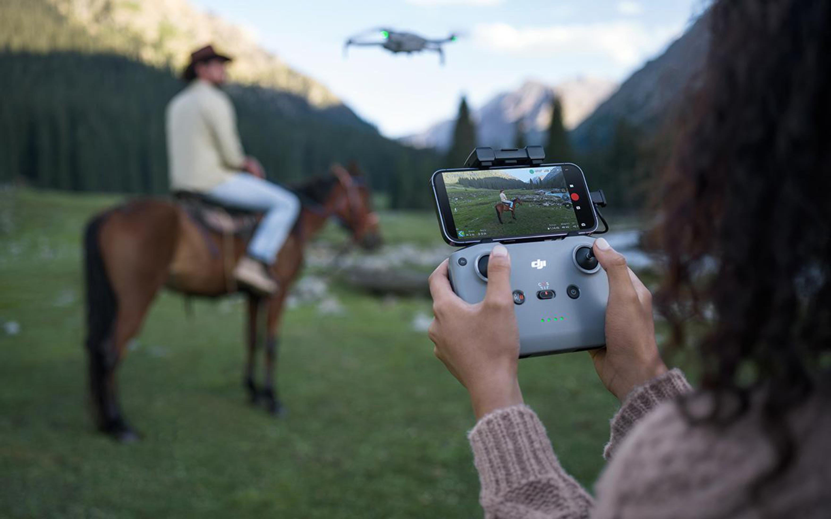 Osoba trzymająca kontroler drona, oglądająca transmisję na żywo kowboja na koniu. Dron na niebie.